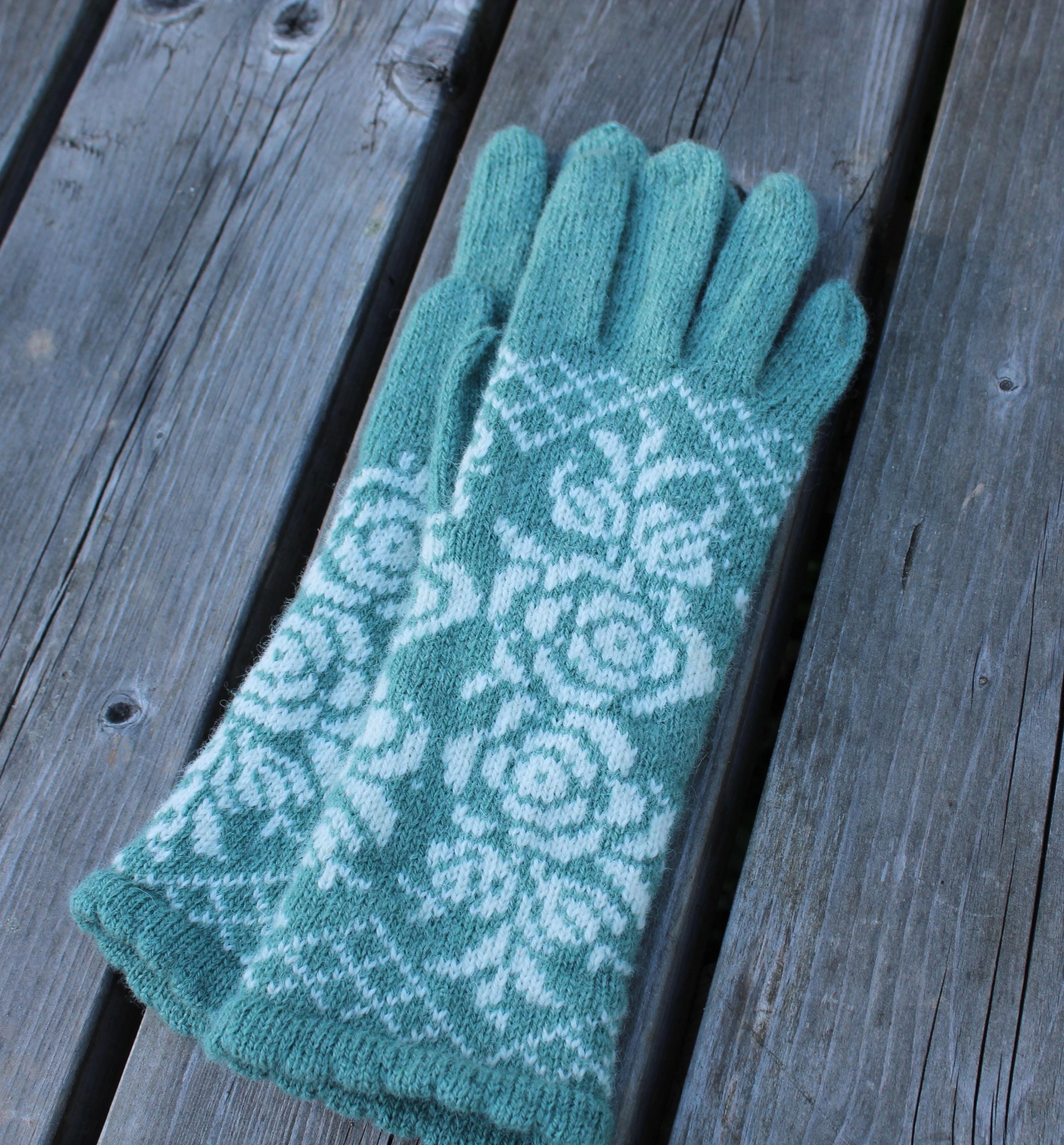 Green knitted gloves with a white pattern on a wooden surface