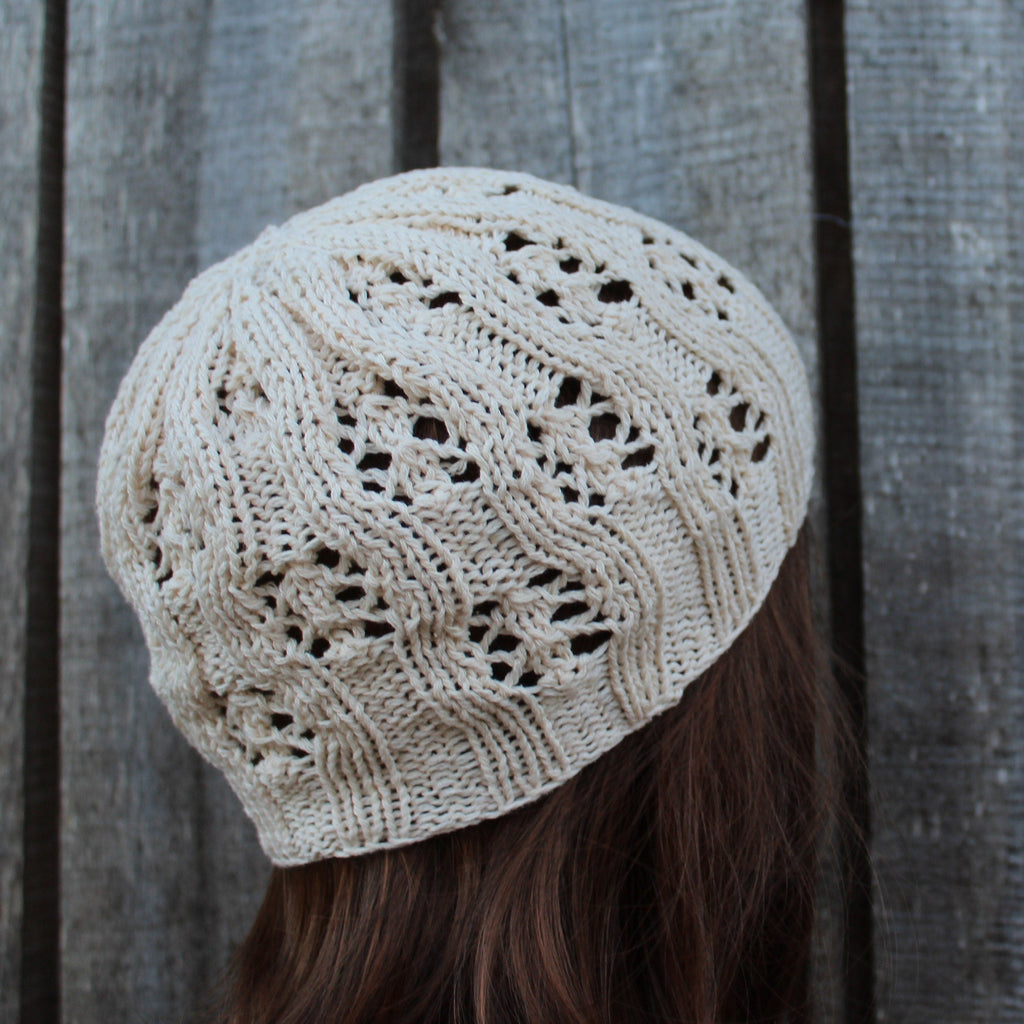 Beige knitted beanie worn by a person against a wooden background