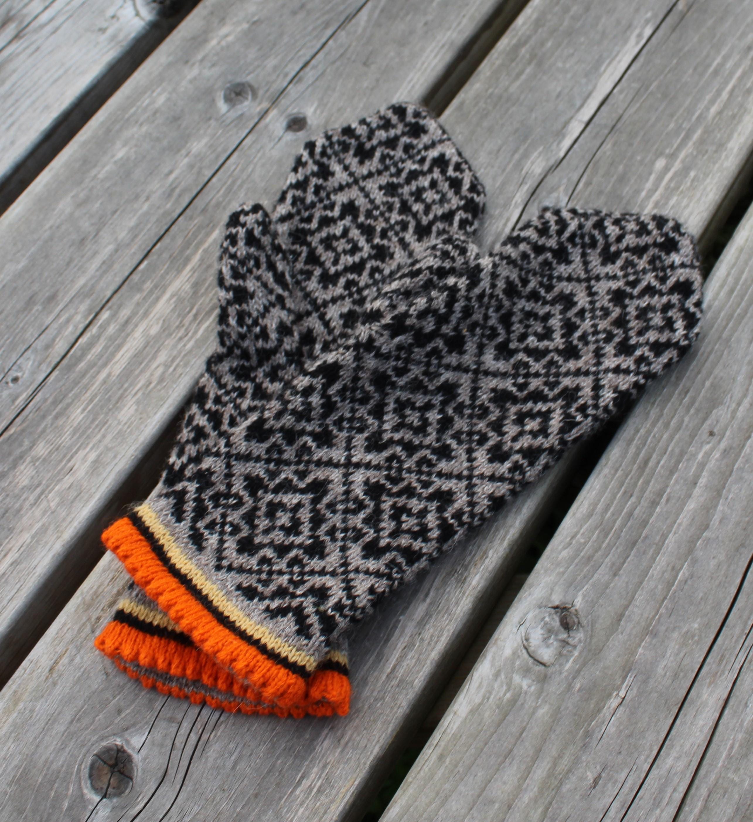 Pair of patterned mittens with orange cuffs on a wooden surface