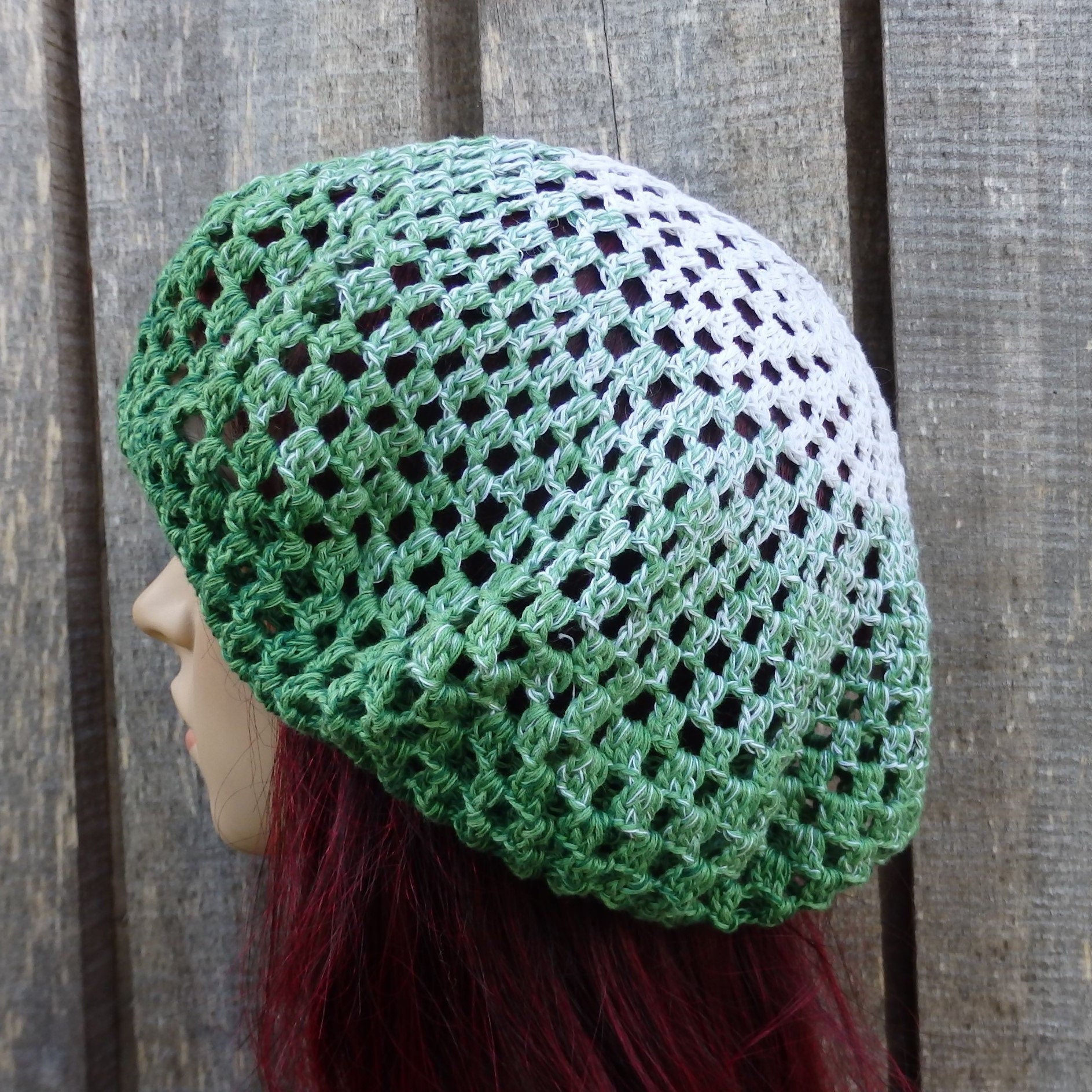 Green and white crocheted hat worn by a mannequin against a wooden background