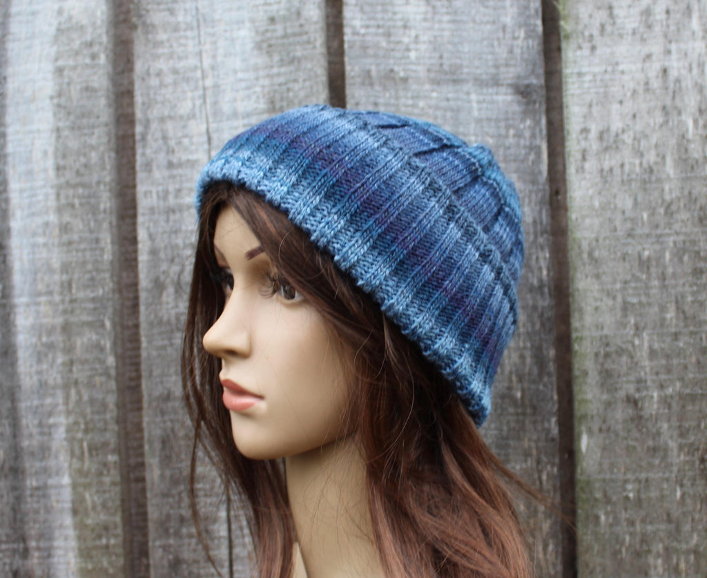 Mannequin head wearing a blue knitted beanie against a wooden fence background