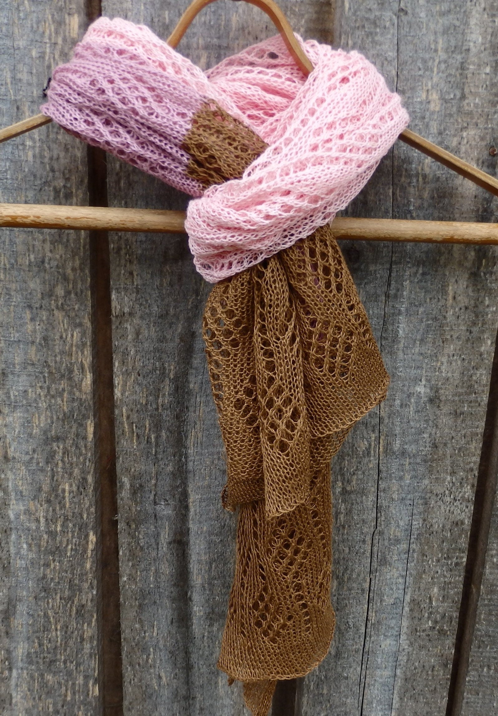 Pink and brown knitted scarves on a wooden hanger against a rustic wooden background