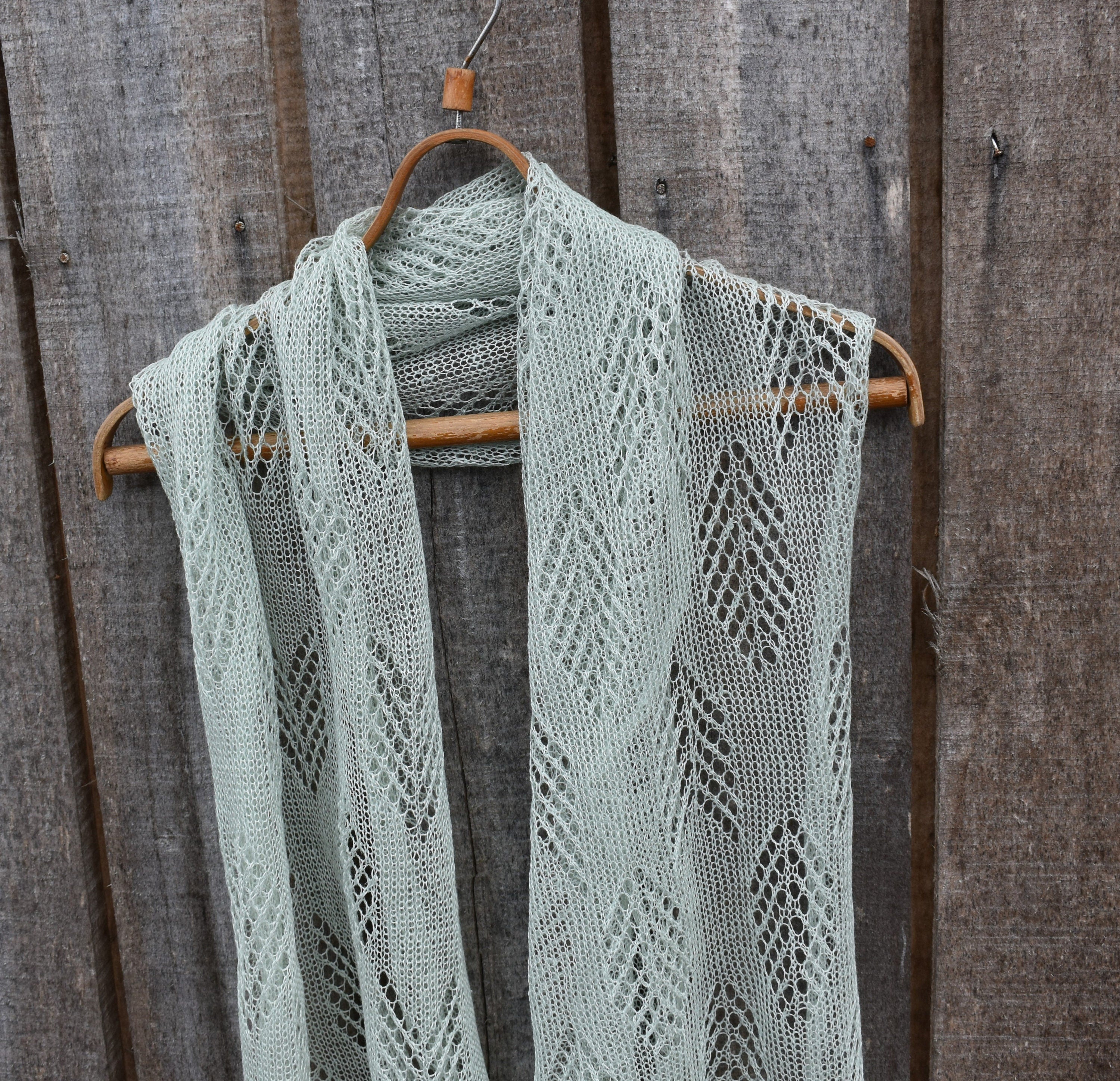 Knitted scarf with a geometric pattern hanging on a wooden hanger against a wooden background