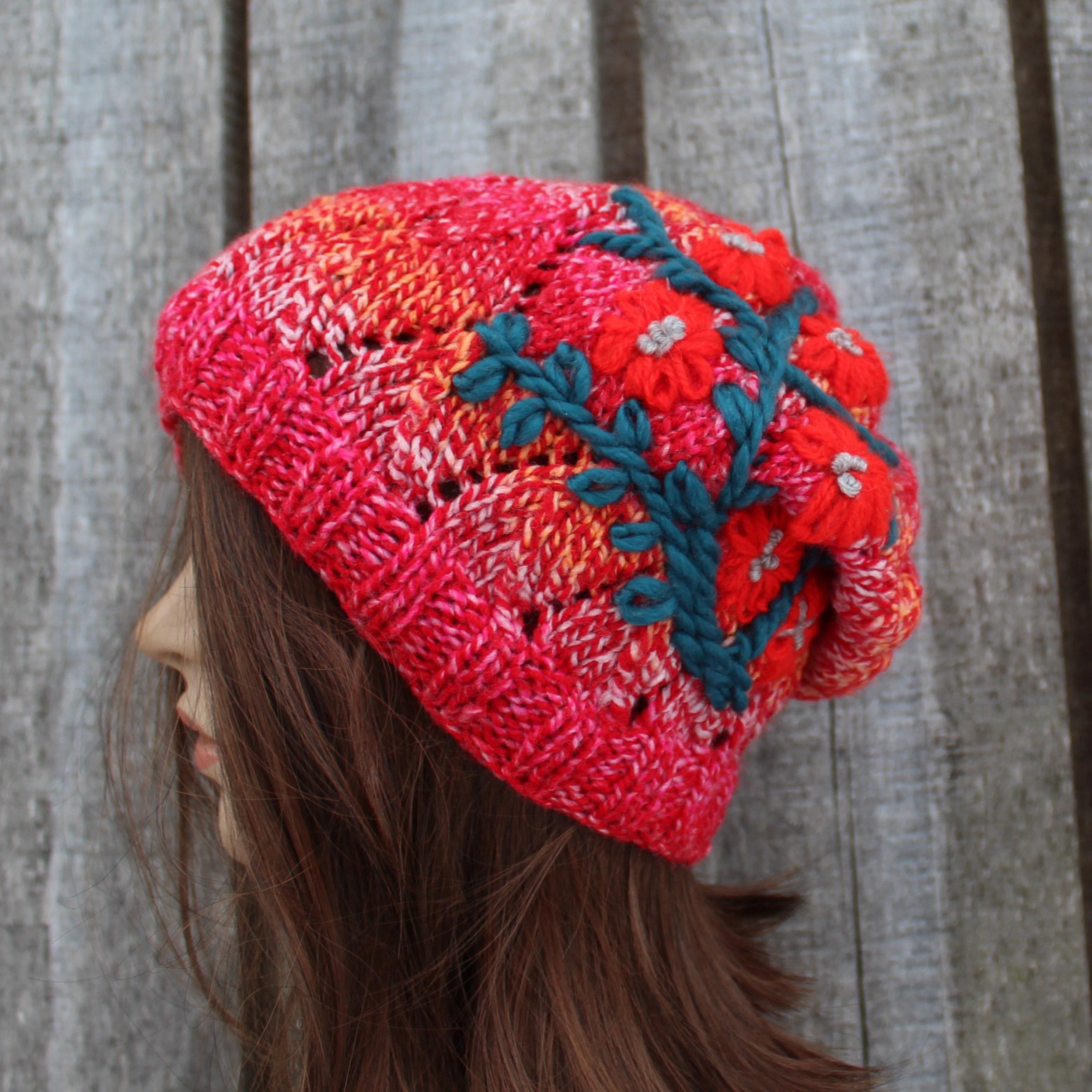 Person wearing a colorful knitted beanie with floral patterns against a wooden background