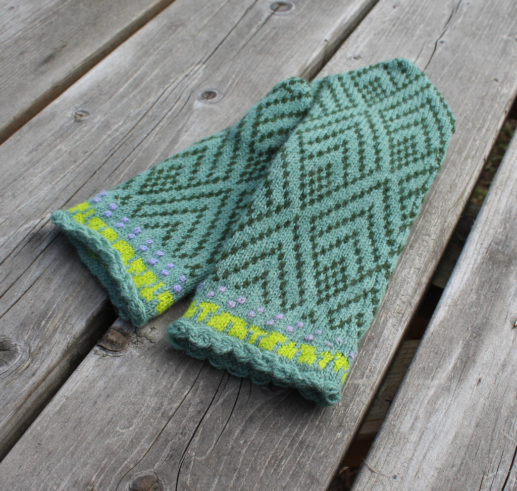 Green knitted mittens with a pattern on a wooden surface