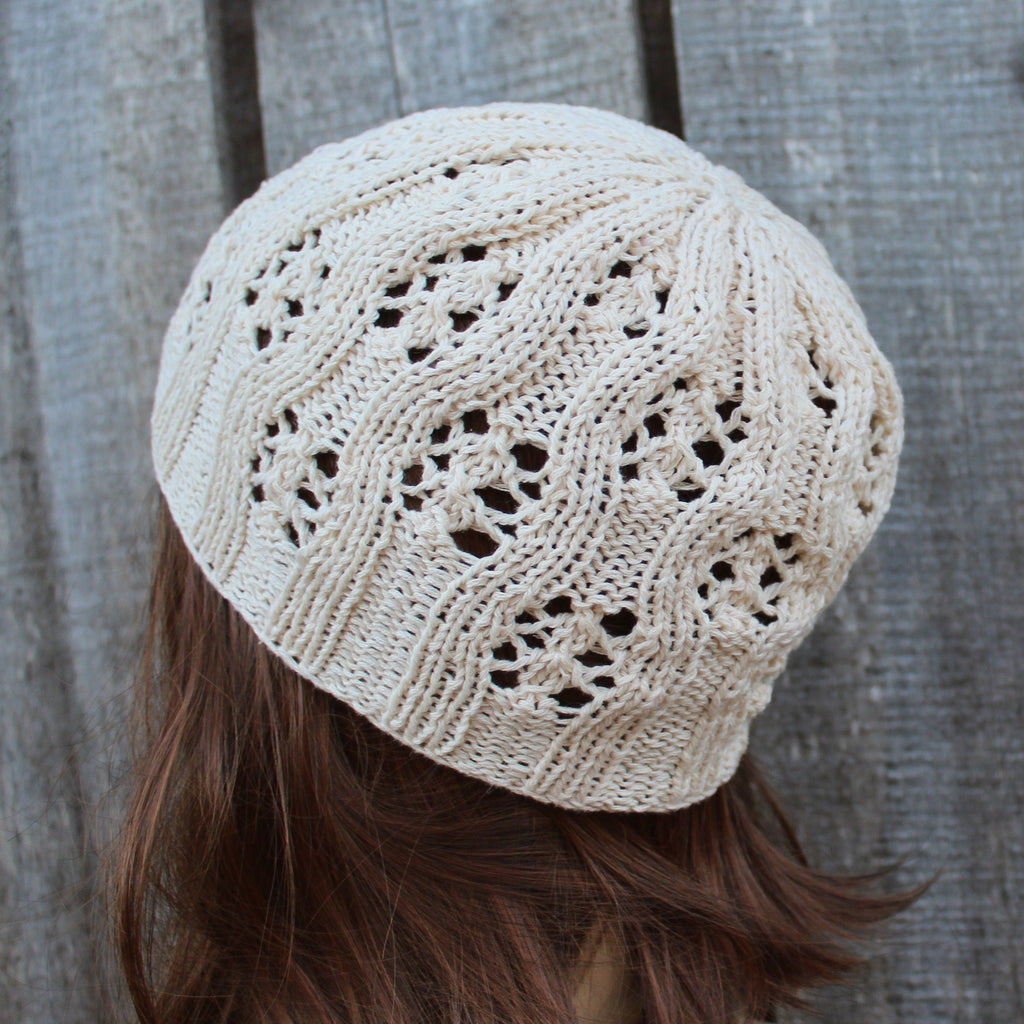 Beige knitted beanie worn by a person with brown hair against a wooden background