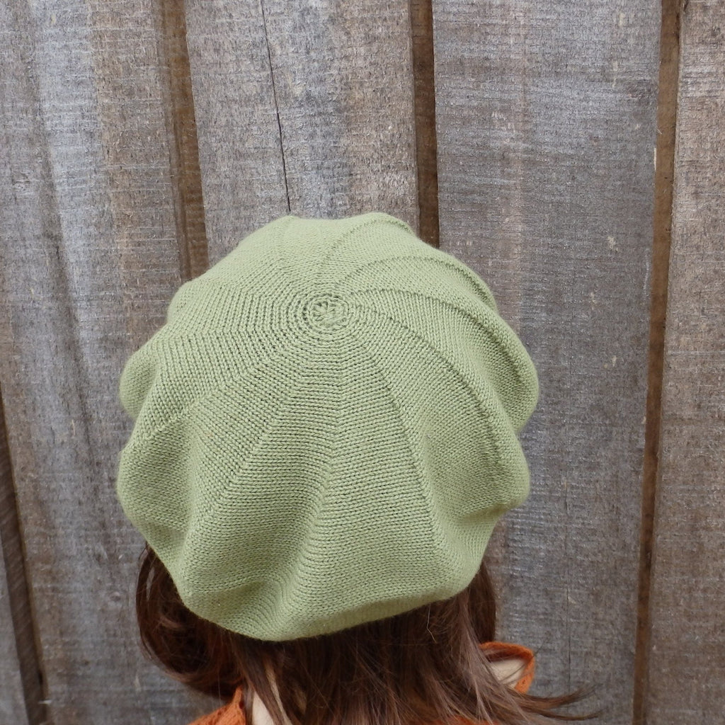 Light green knitted beret worn by a person against a wooden background