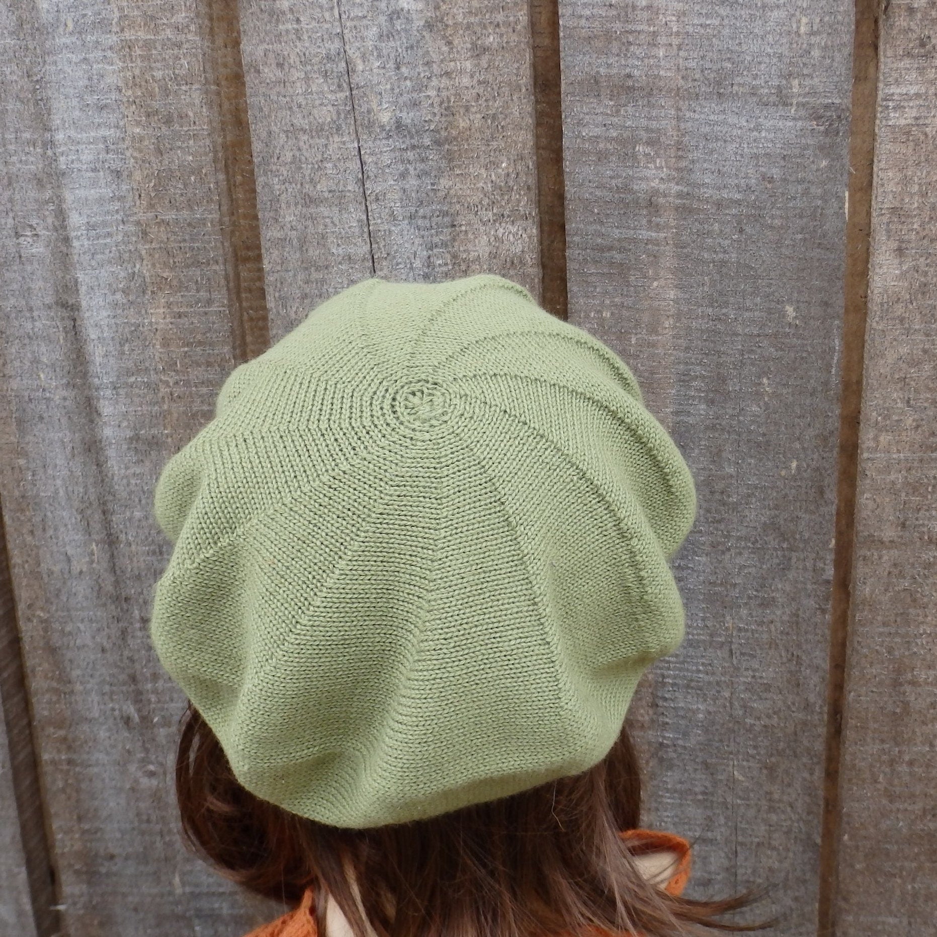 Light green knitted beret worn by a person against a wooden background