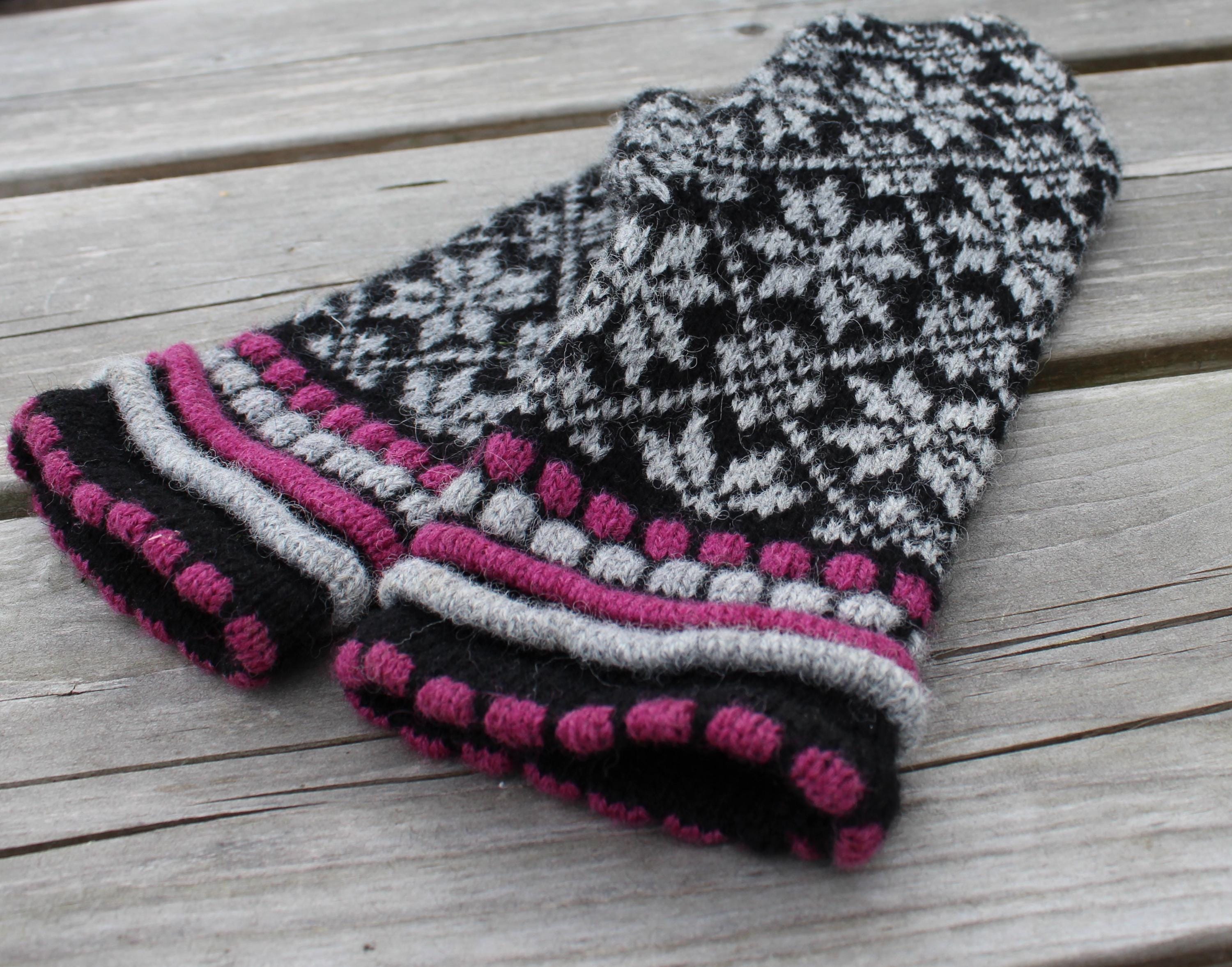 Knitted dog sweater with black, gray, and pink pattern on a wooden surface