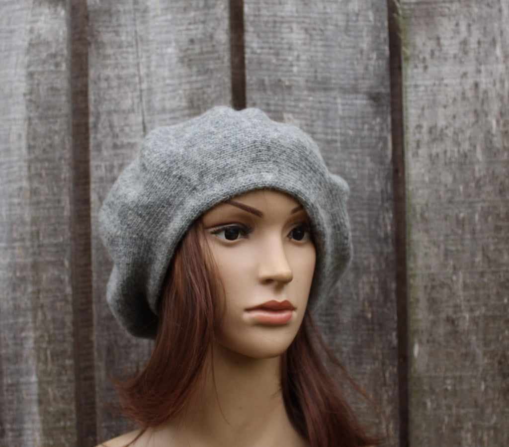 Mannequin head wearing a gray beret against a wooden panel background