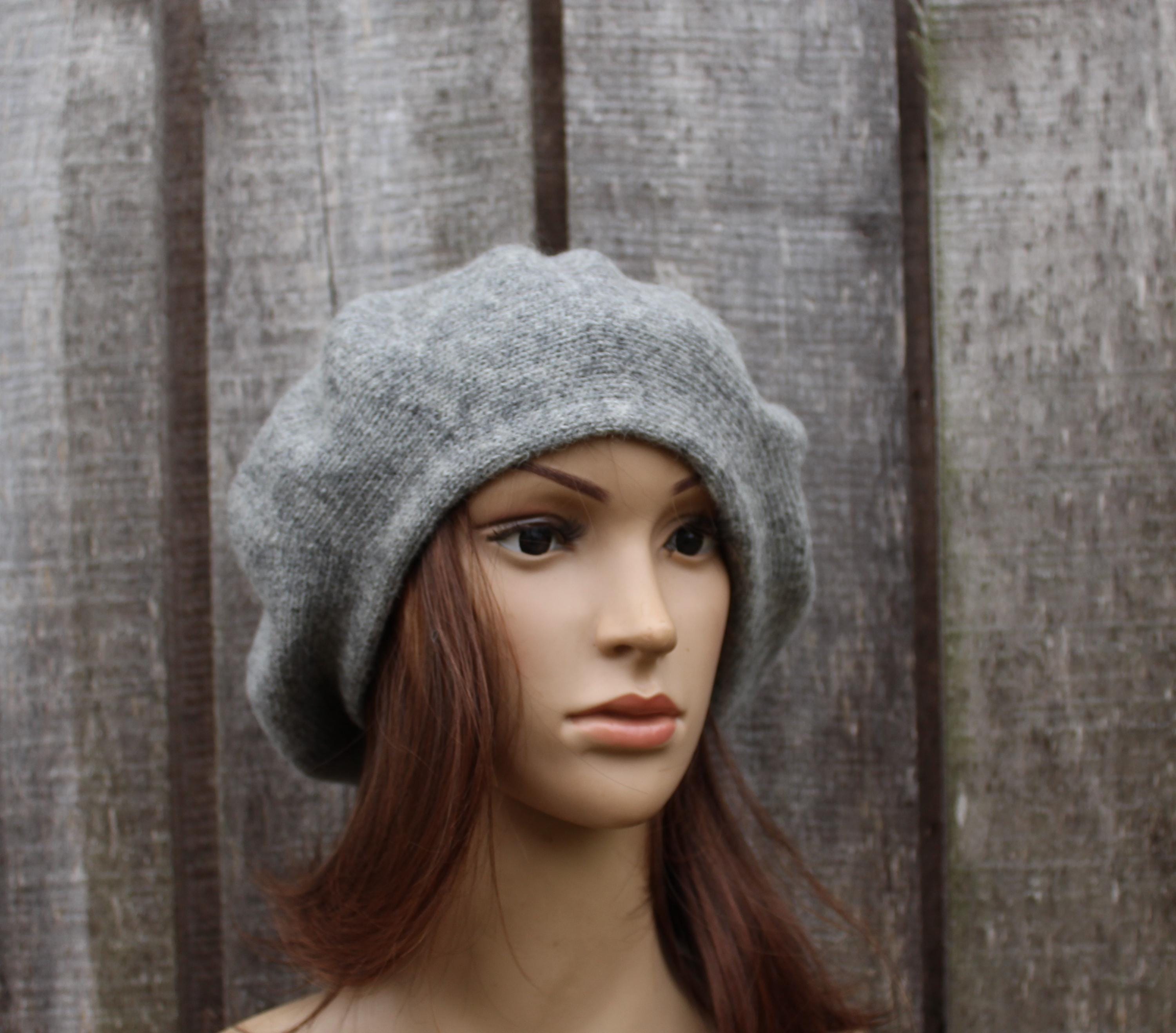 Mannequin head wearing a gray beret against a wooden panel background