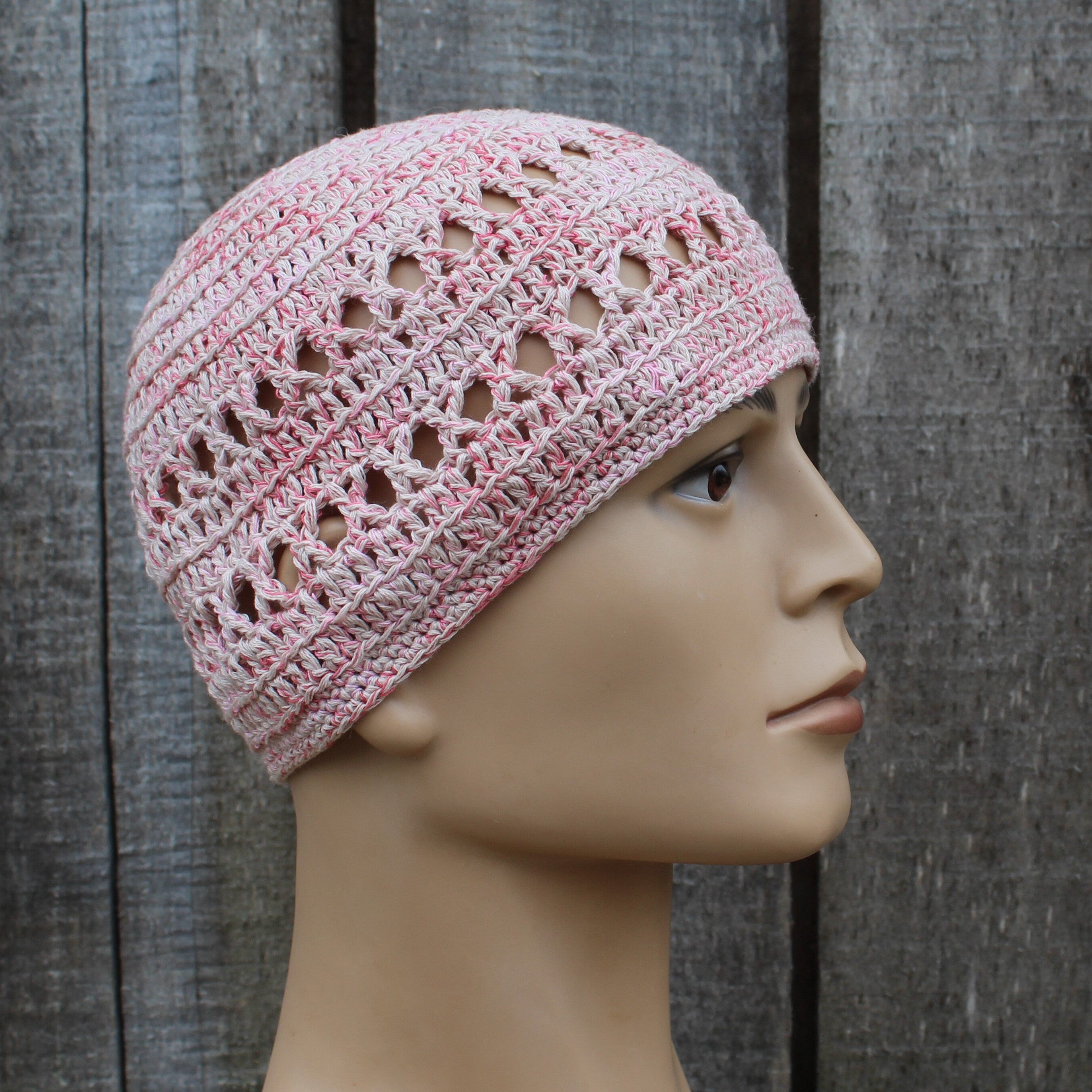Pink crochet hat on a mannequin head against a wooden background