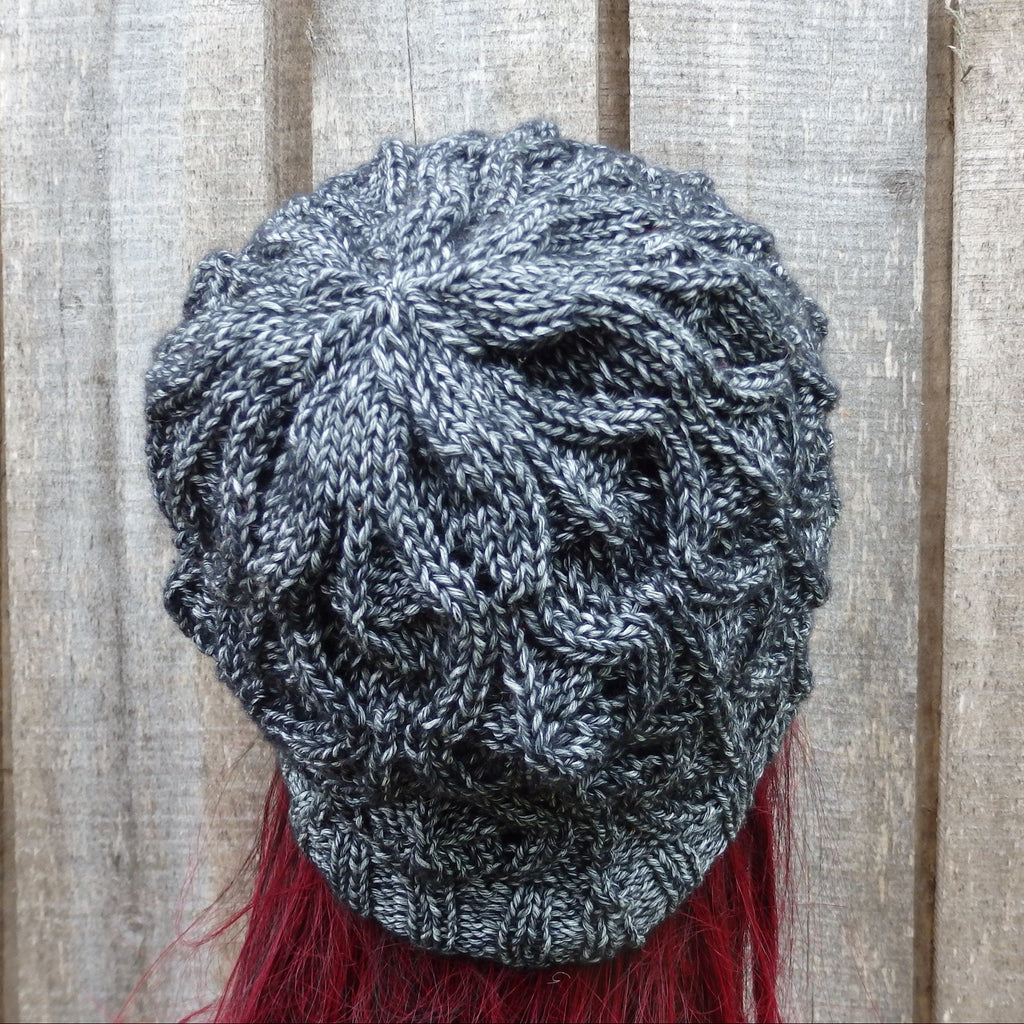 Knitted gray beanie with red tassels on a wooden background