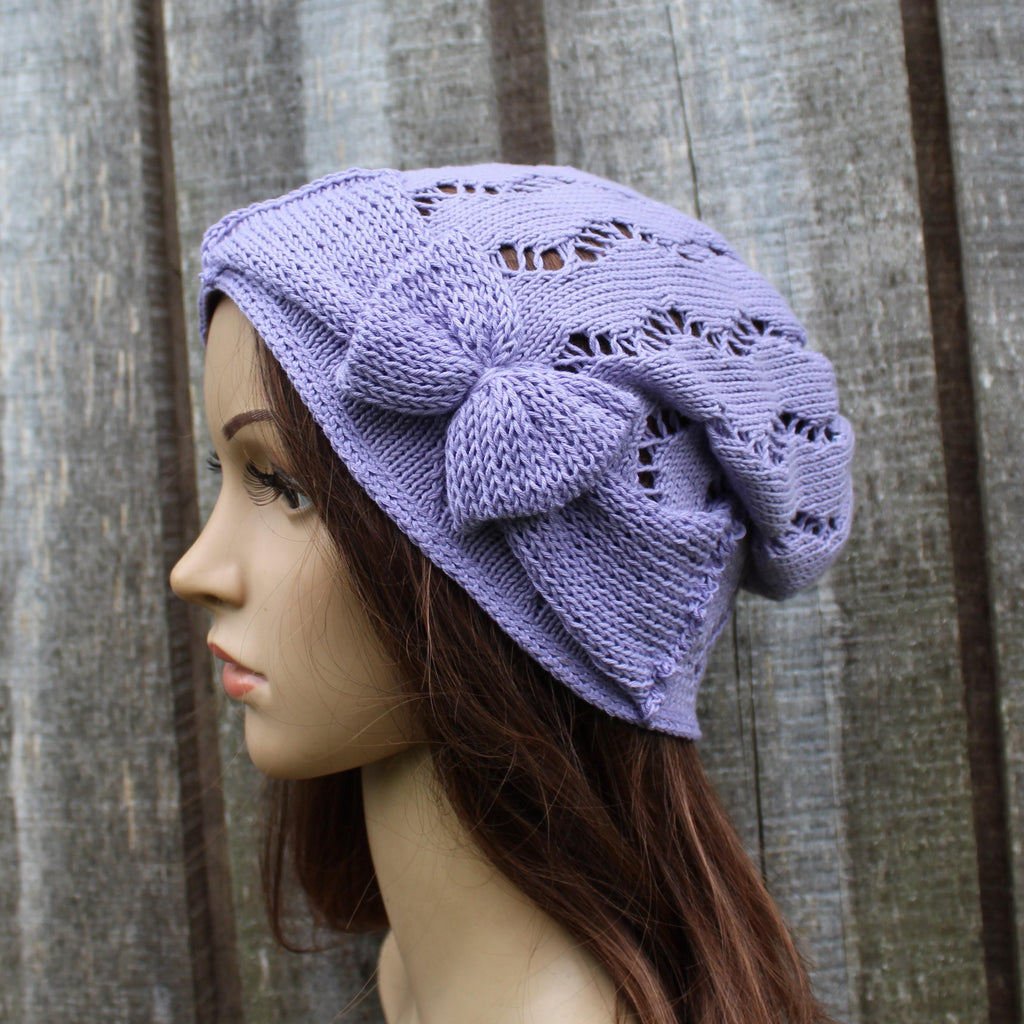 Lavender knitted hat with a bow on a mannequin head against a wooden background