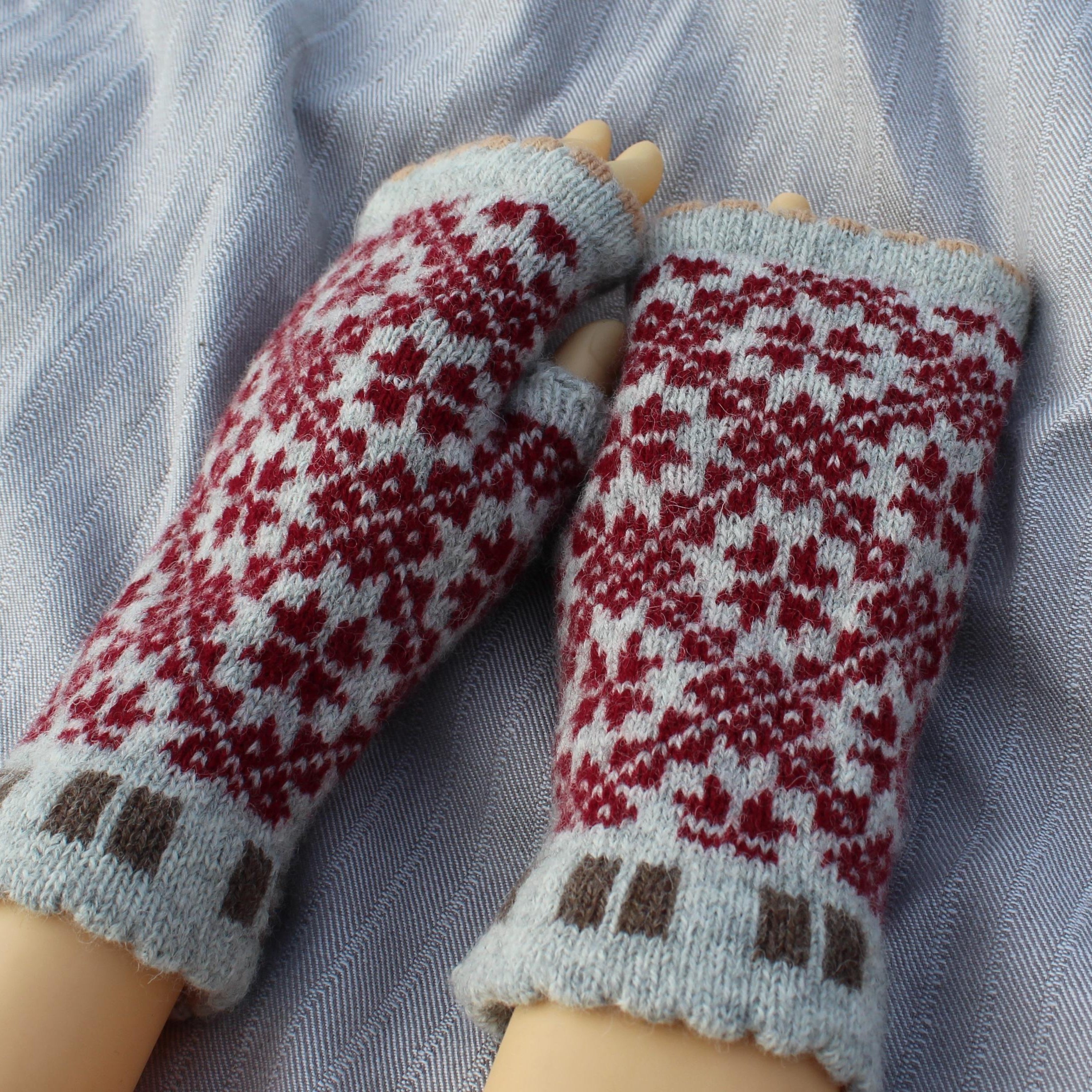 Pair of knitted mittens with a red and white pattern on a light blue fabric background.