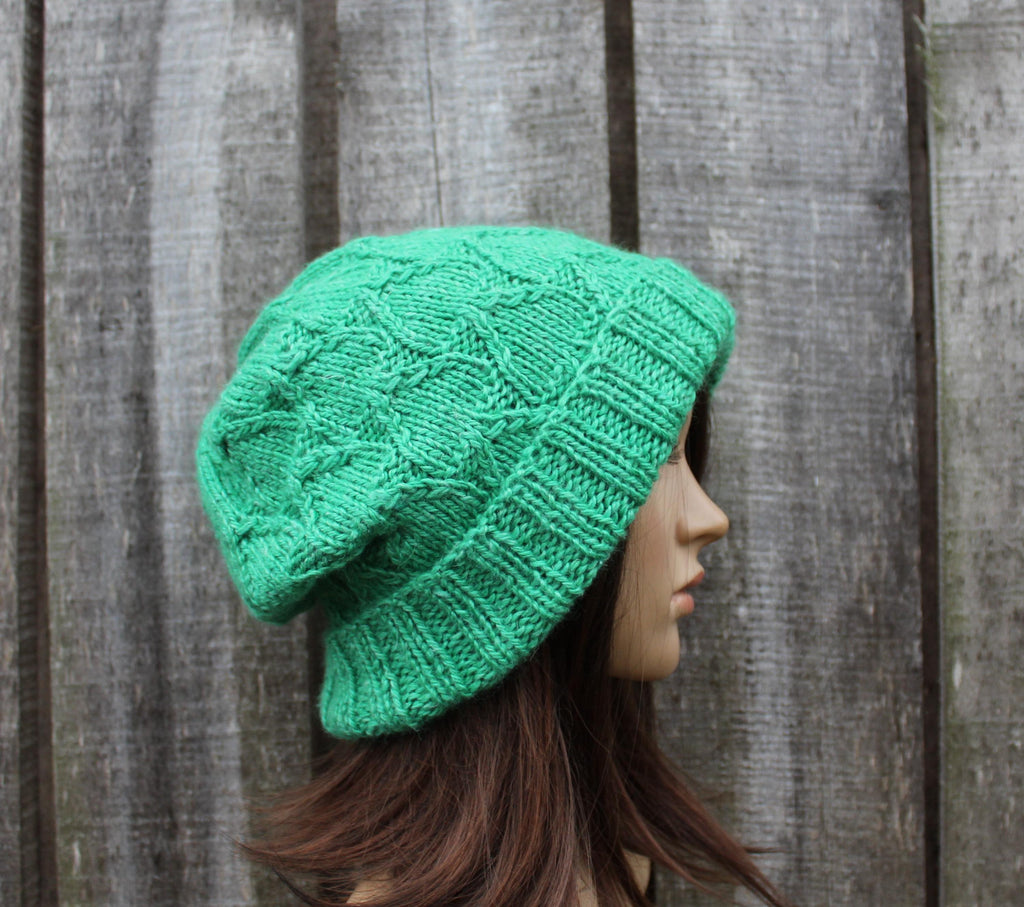 Green knitted beanie worn by a mannequin against a wooden background