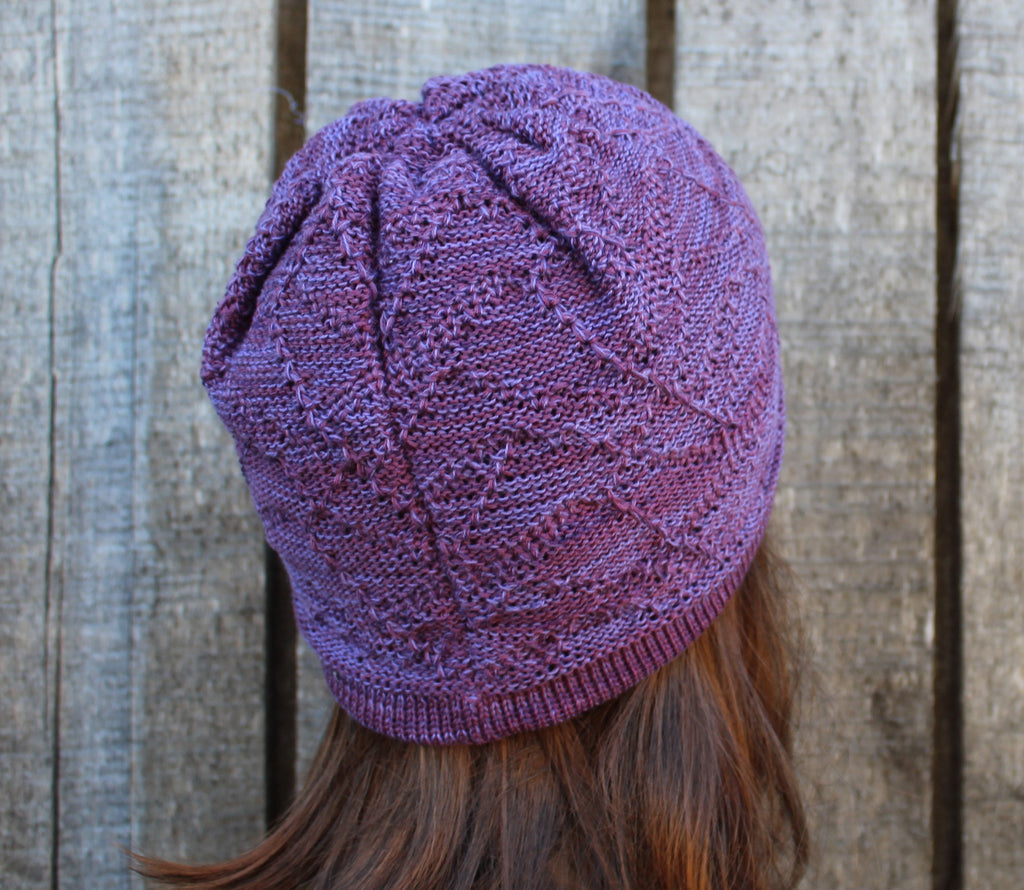 Purple knitted beanie worn by a person with wooden planks in the background