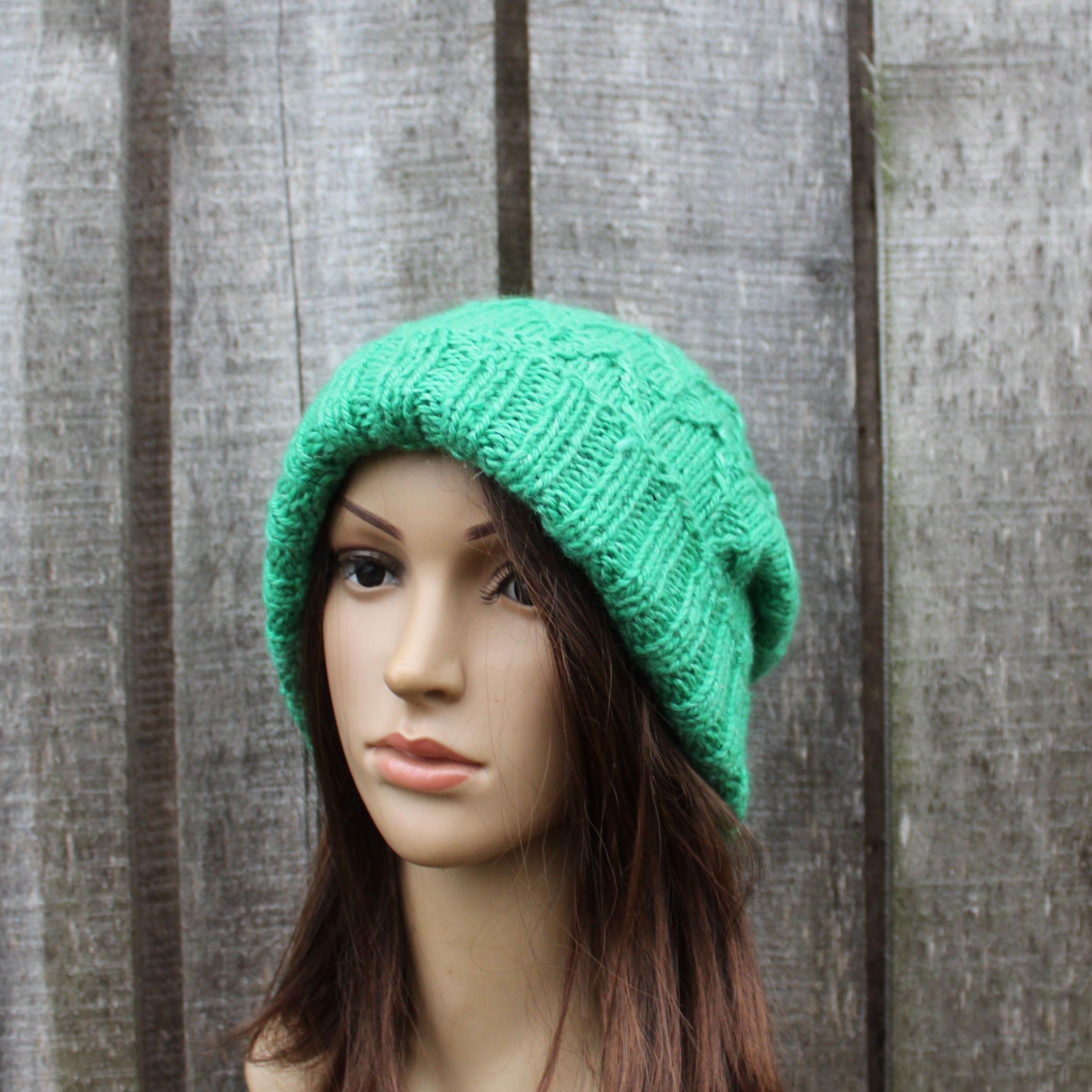 Green knitted beanie on a mannequin head against a wooden background