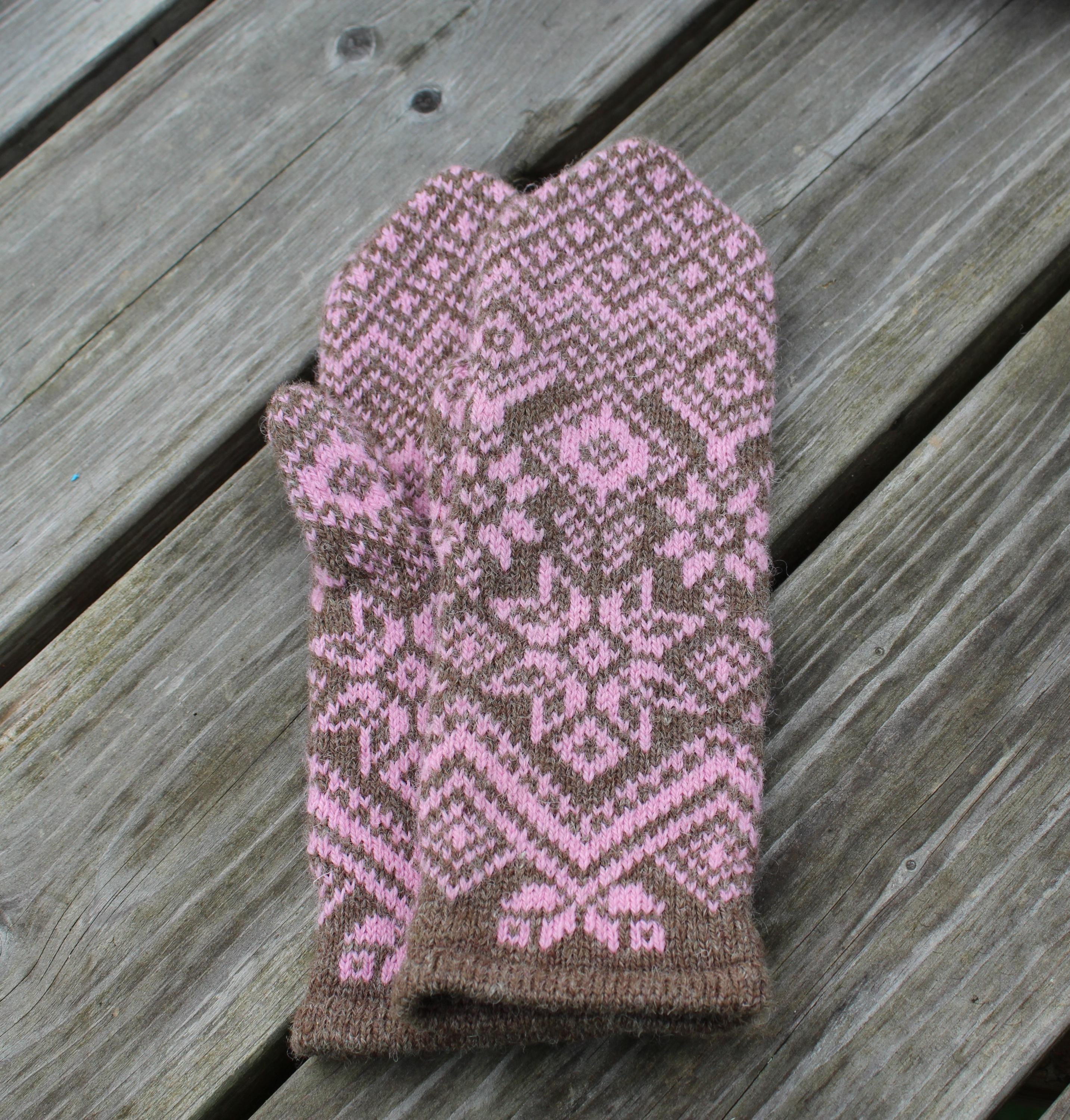 Knitted mittens with pink and brown pattern on a wooden surface