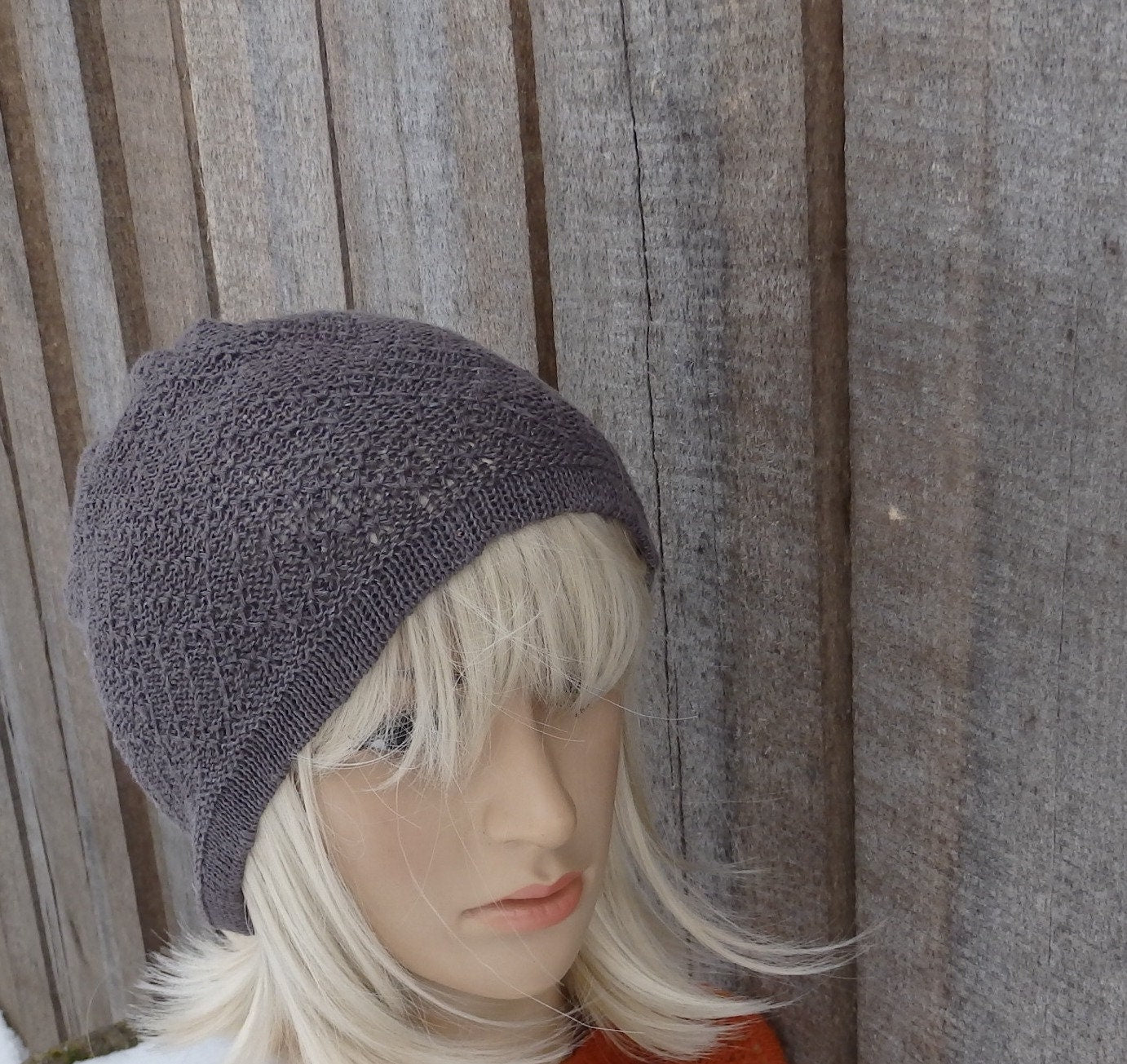 Mannequin head wearing a knitted gray beanie against a wooden fence background