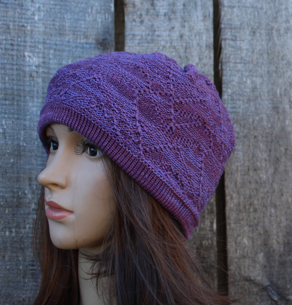 Purple knitted hat on a mannequin head against a textured wall.
