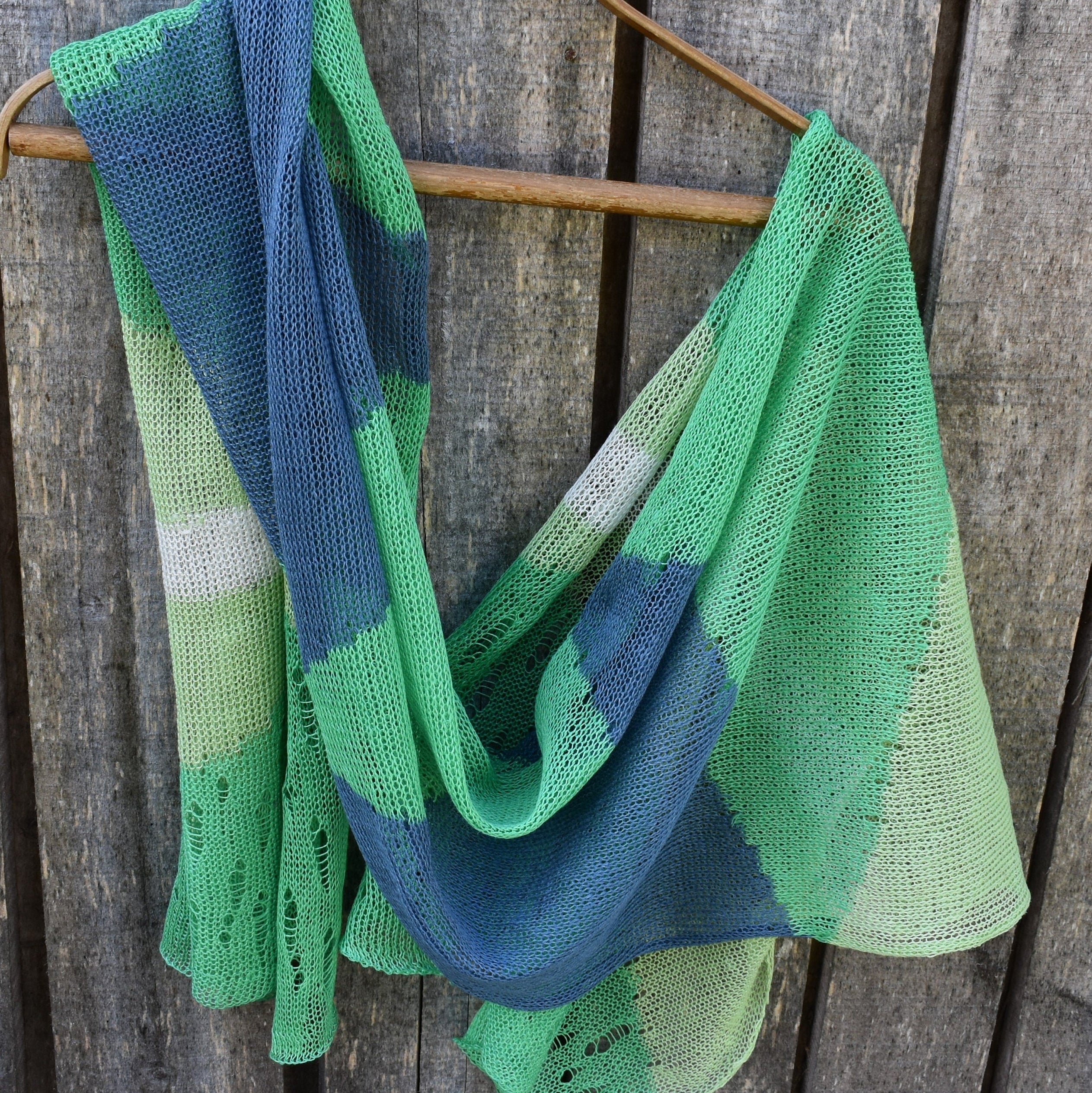 Green and blue knitted shawl on a wooden hanger against a wooden background