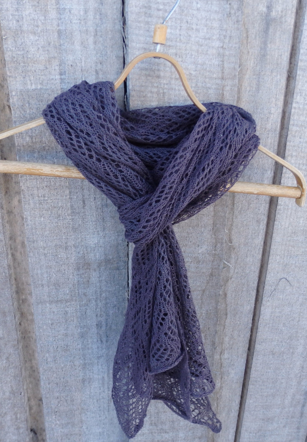 Purple knitted scarf on a wooden hanger against a wooden background