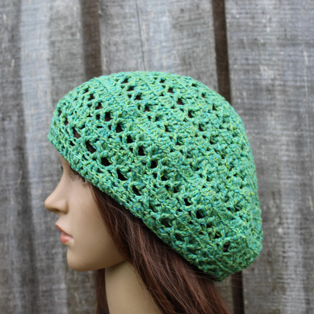 Green crocheted beret on a mannequin head against a wooden background