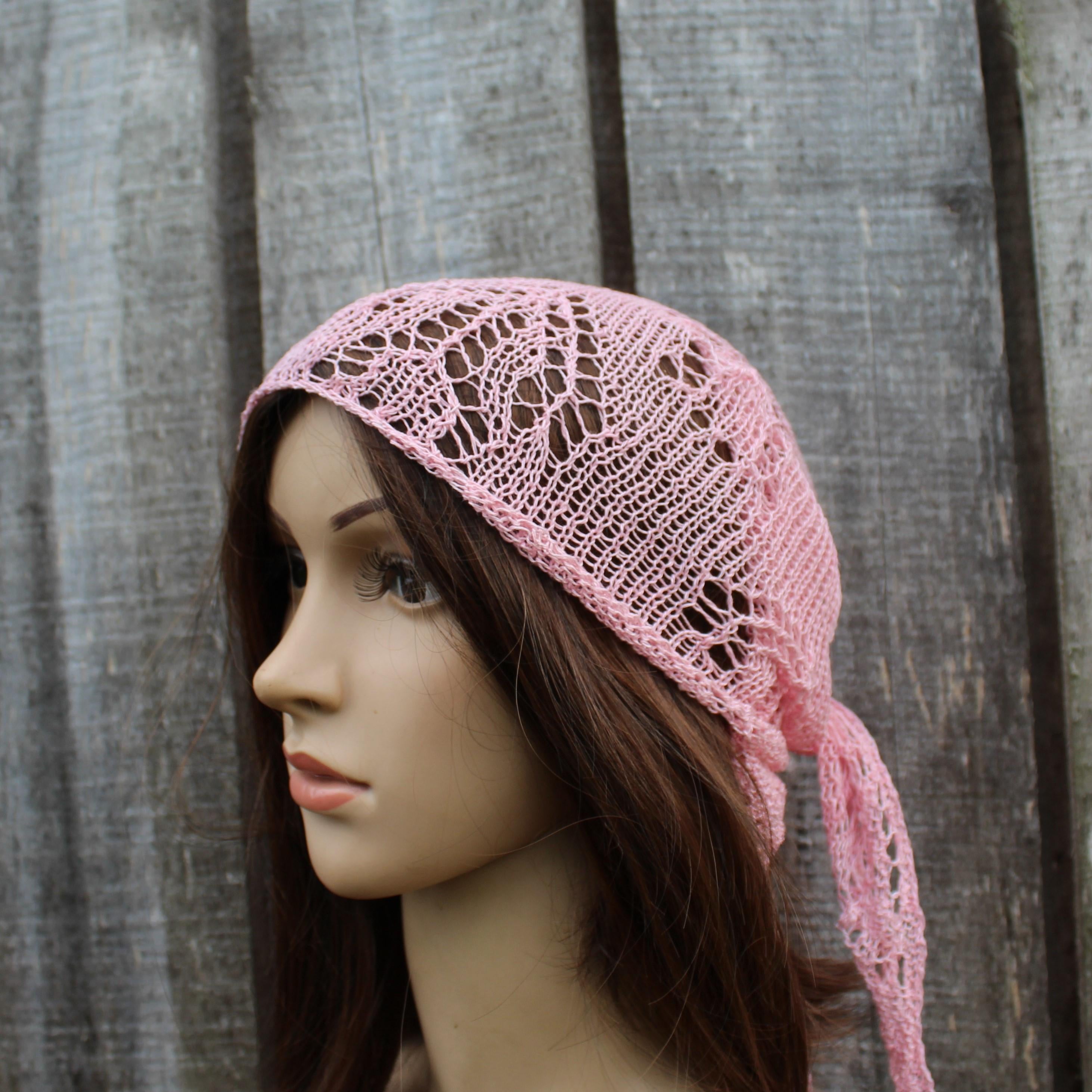 Mannequin head wearing a pink knitted headscarf against a wooden background