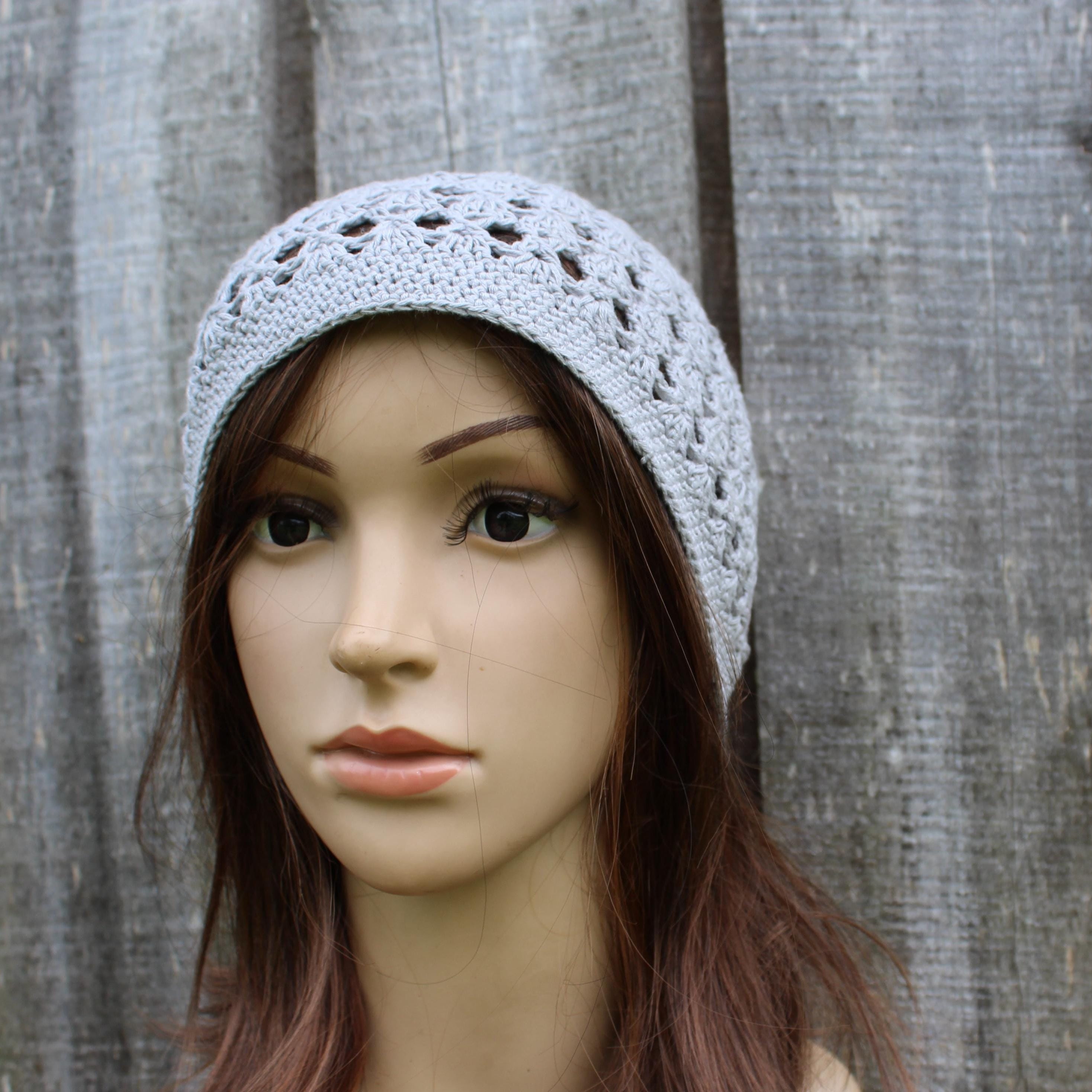 Mannequin head wearing a gray crochet beanie against a wooden background