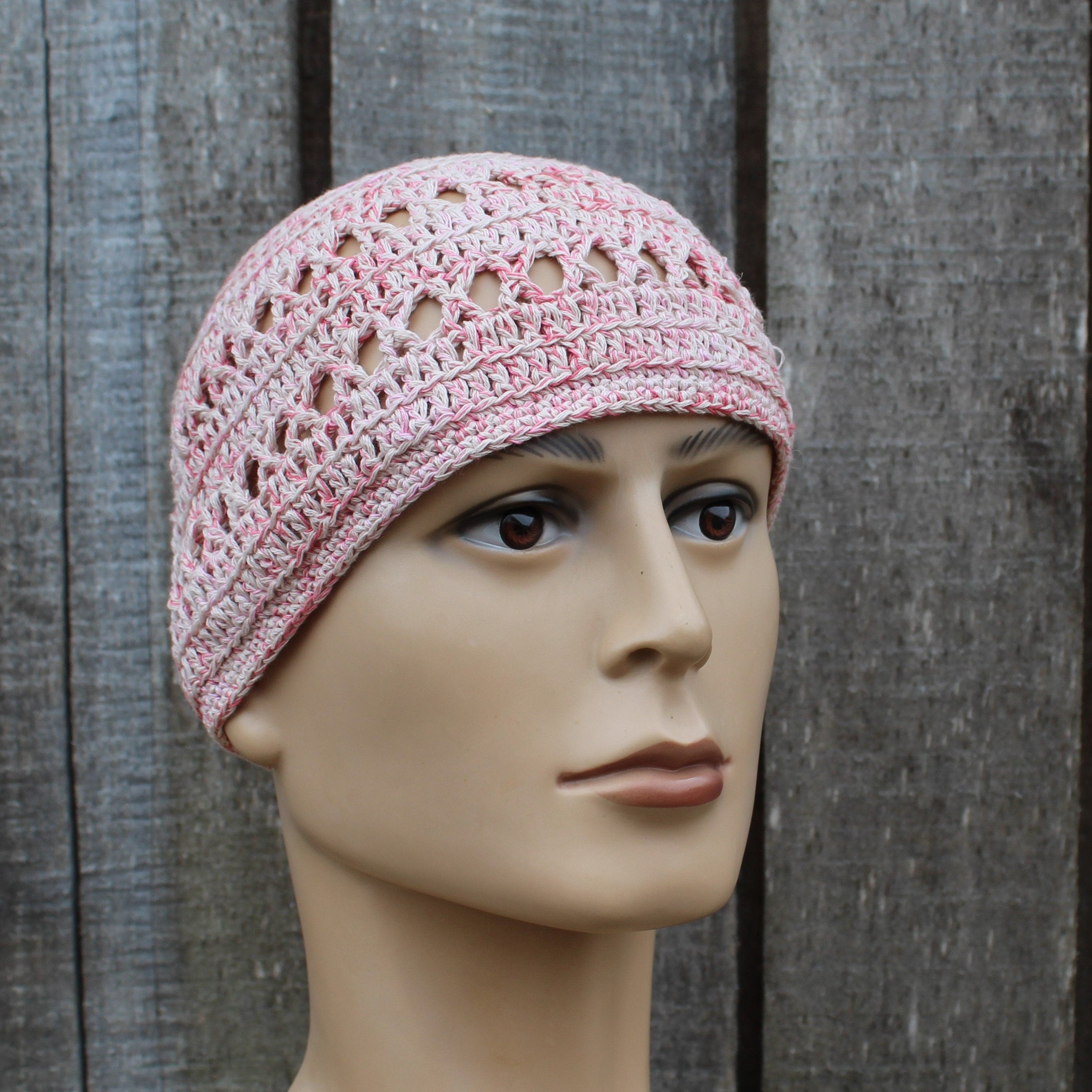 Pink crochet hat on a mannequin head against a wooden background