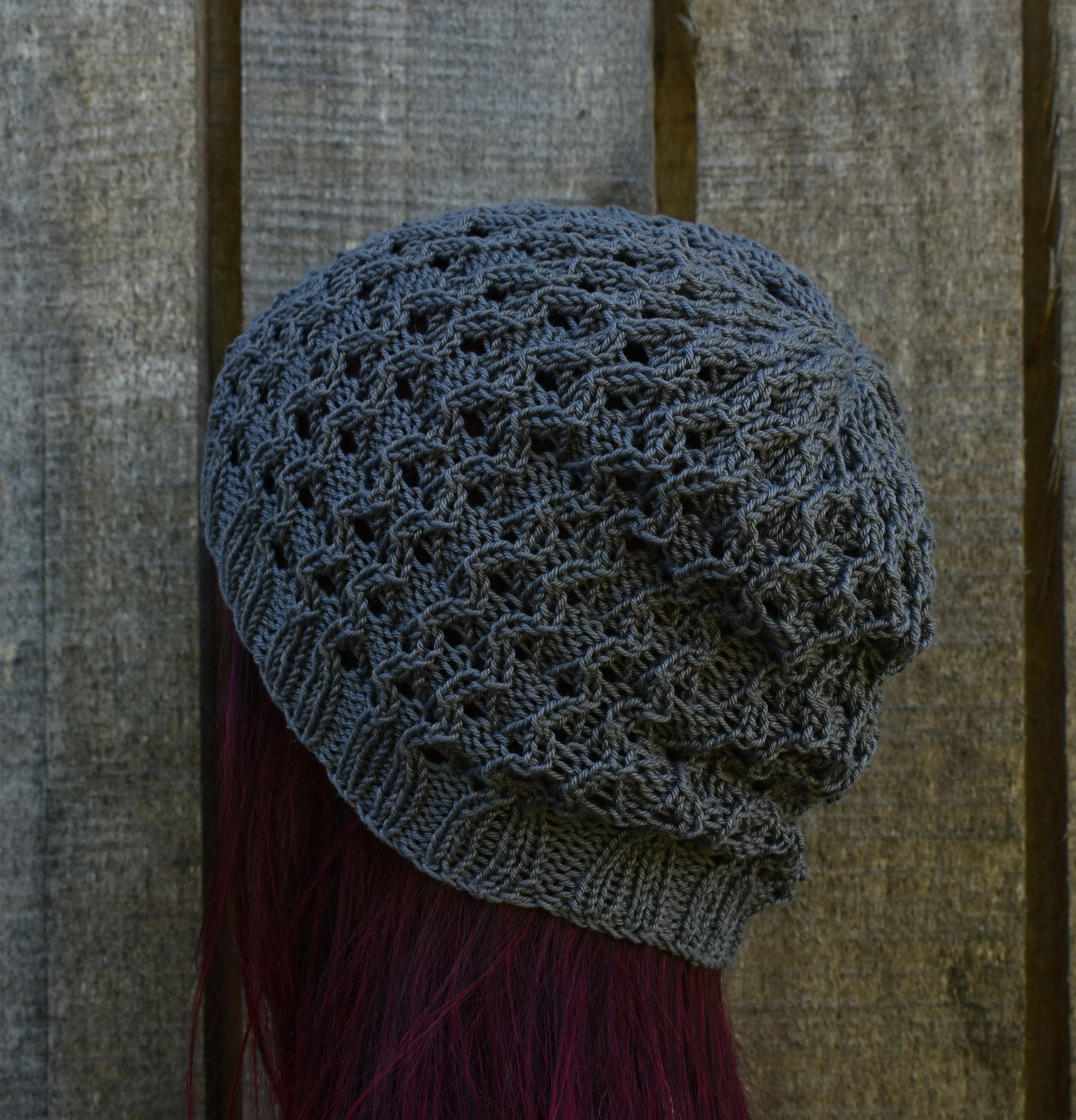 Knitted gray beanie on a person with red hair against a wooden background