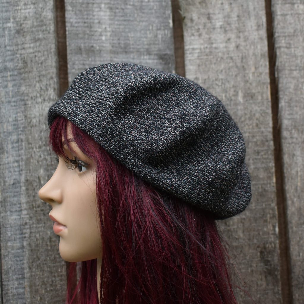 Mannequin head wearing a black knit beret against a wooden background