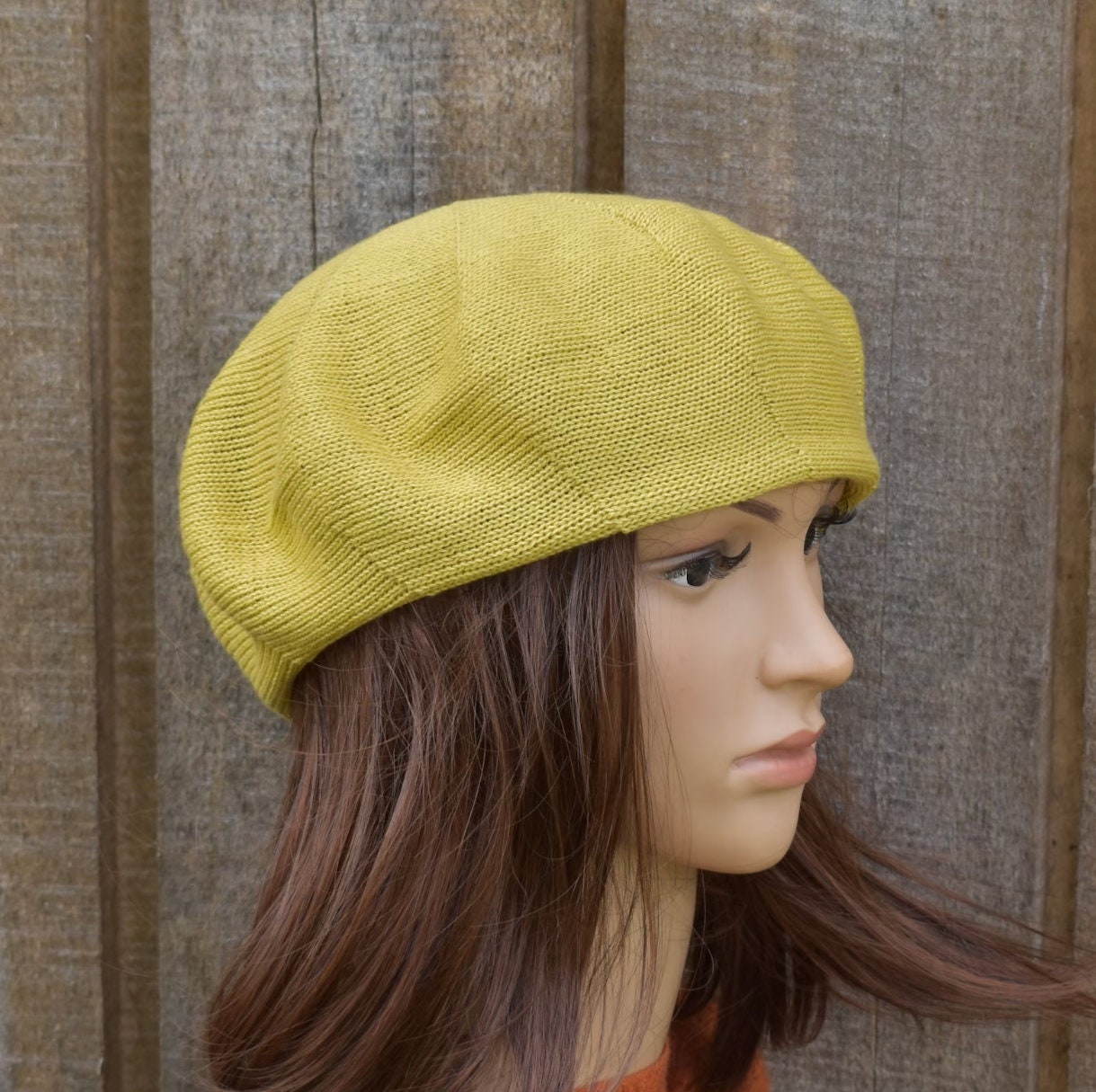 Yellow knit beret on a mannequin head against a wooden panel background