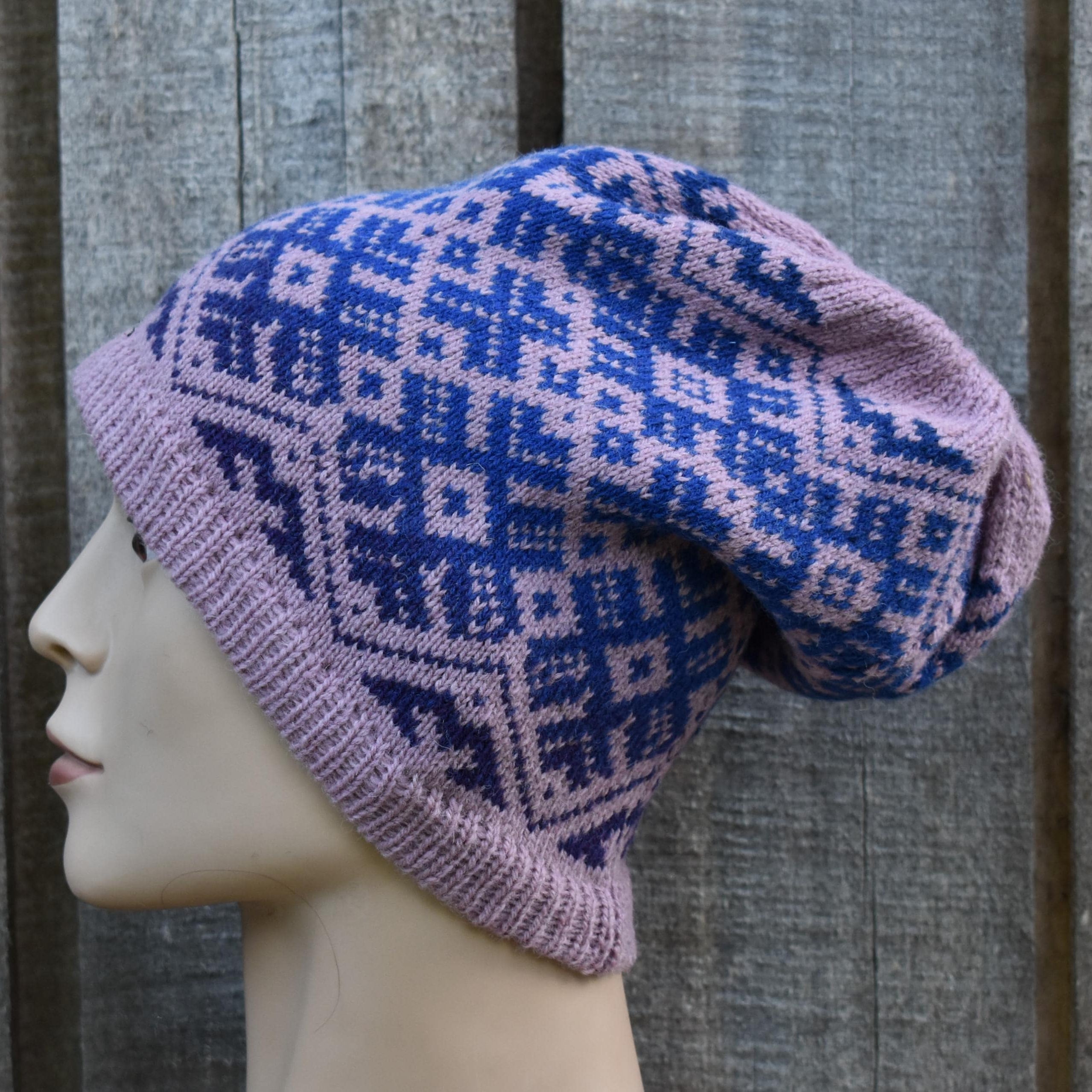 Knitted hat with a blue and pink pattern on a mannequin head against a wooden background