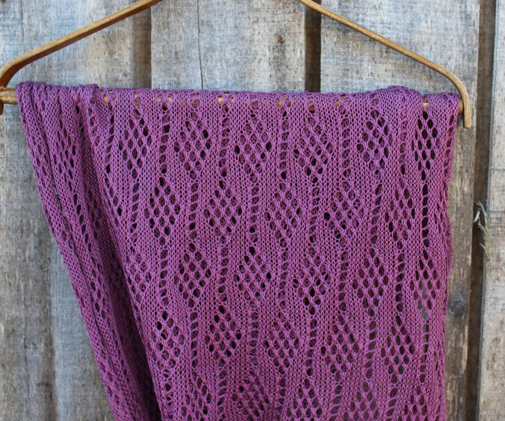 Purple knitted shawl on a wooden hanger against a rustic wooden background