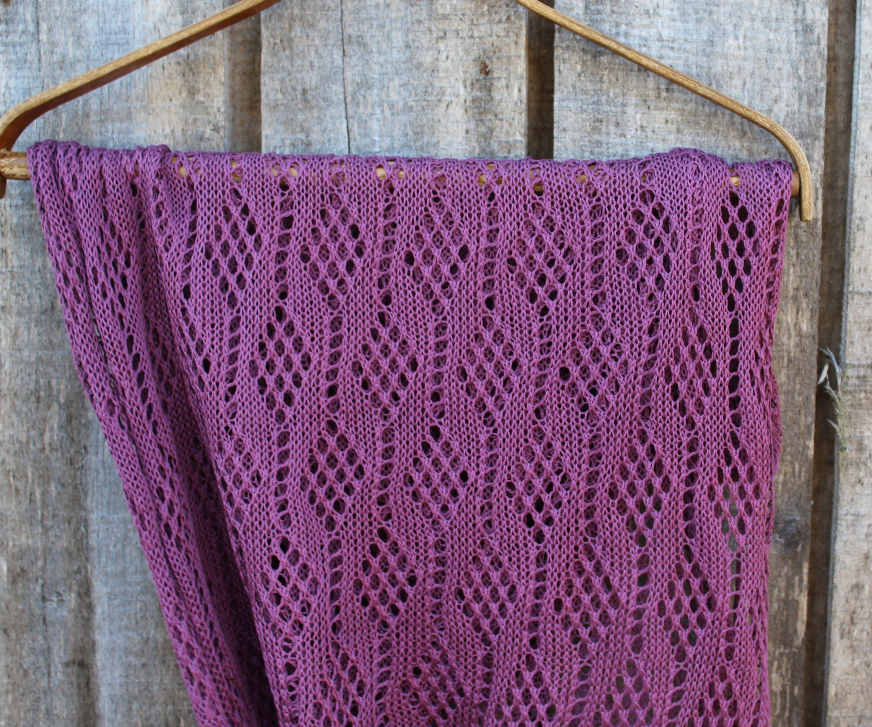 Purple knitted shawl on a wooden hanger against a rustic wooden background
