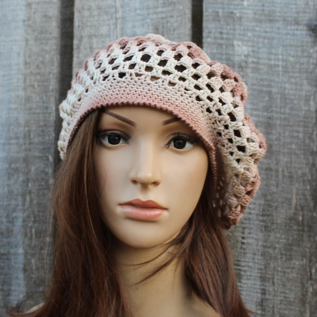 Mannequin head wearing a crocheted pink and beige hat against a wooden background