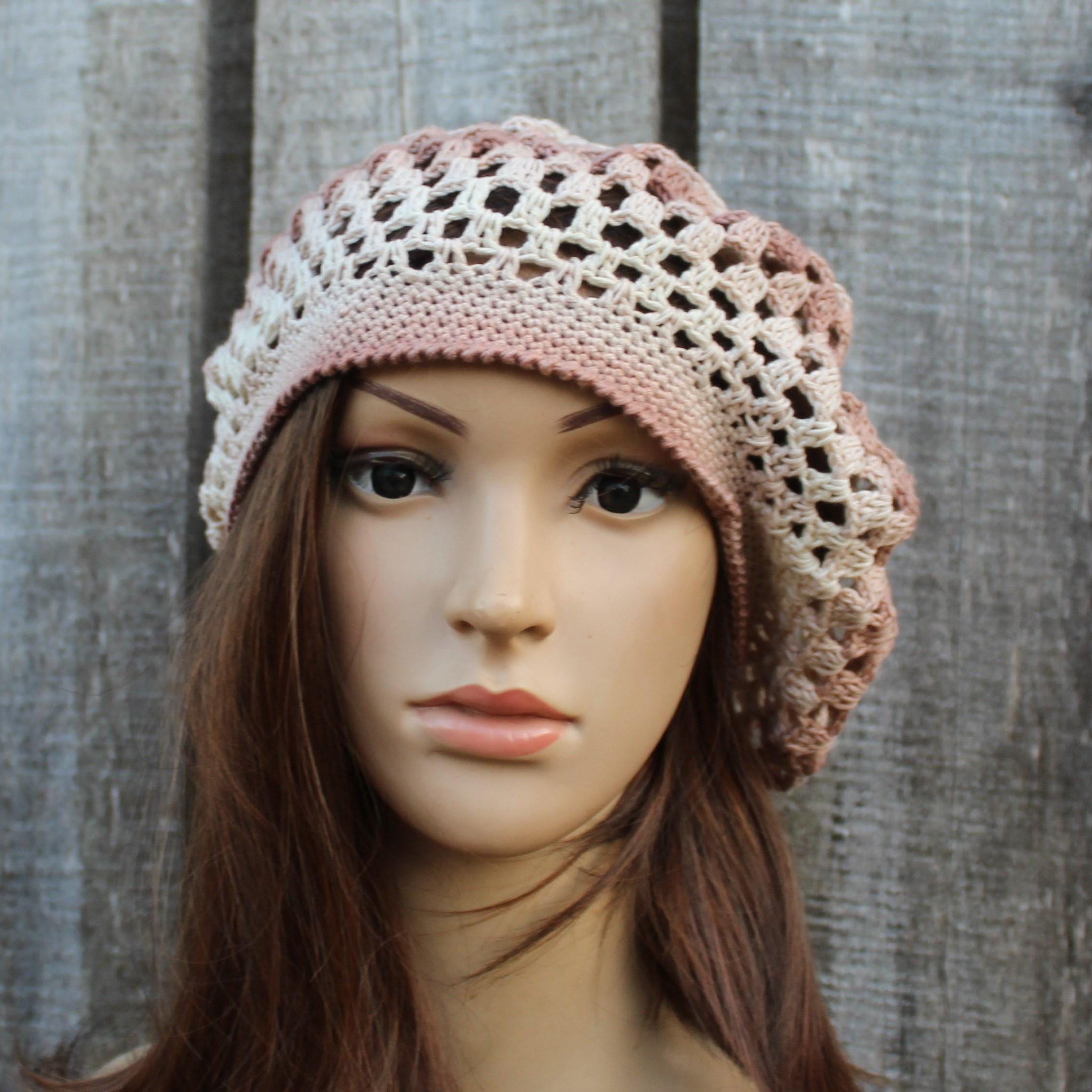 Mannequin head wearing a crocheted pink and beige hat against a wooden background