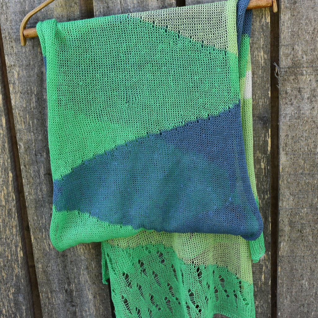 Green and blue knitted shawl hanging on a wooden surface