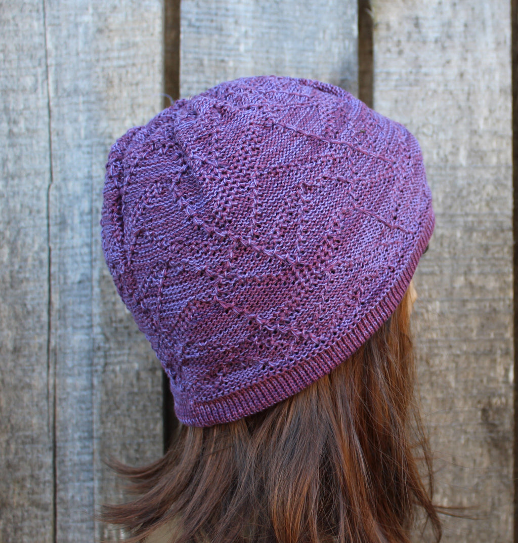 Purple knitted hat worn by a person against a wooden background