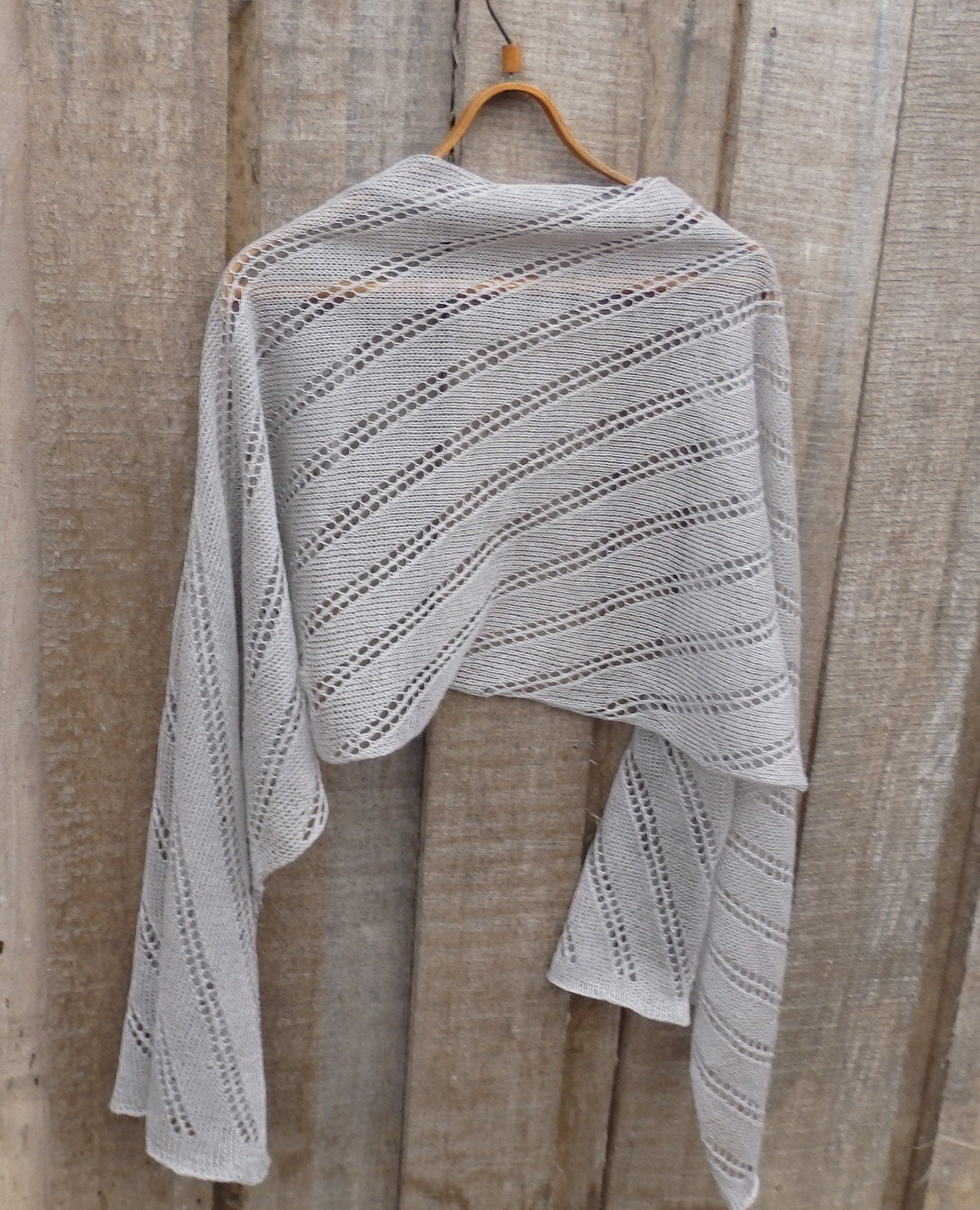 Knitted shawl draped over a wooden hanger against a wooden background