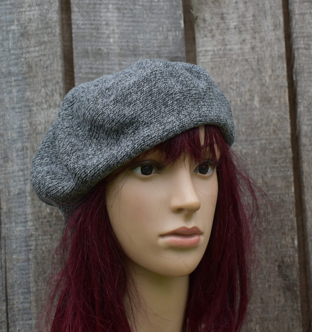 Mannequin head wearing a gray knit beret against a wooden background