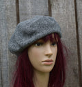 Mannequin head wearing a gray knit beret against a wooden background