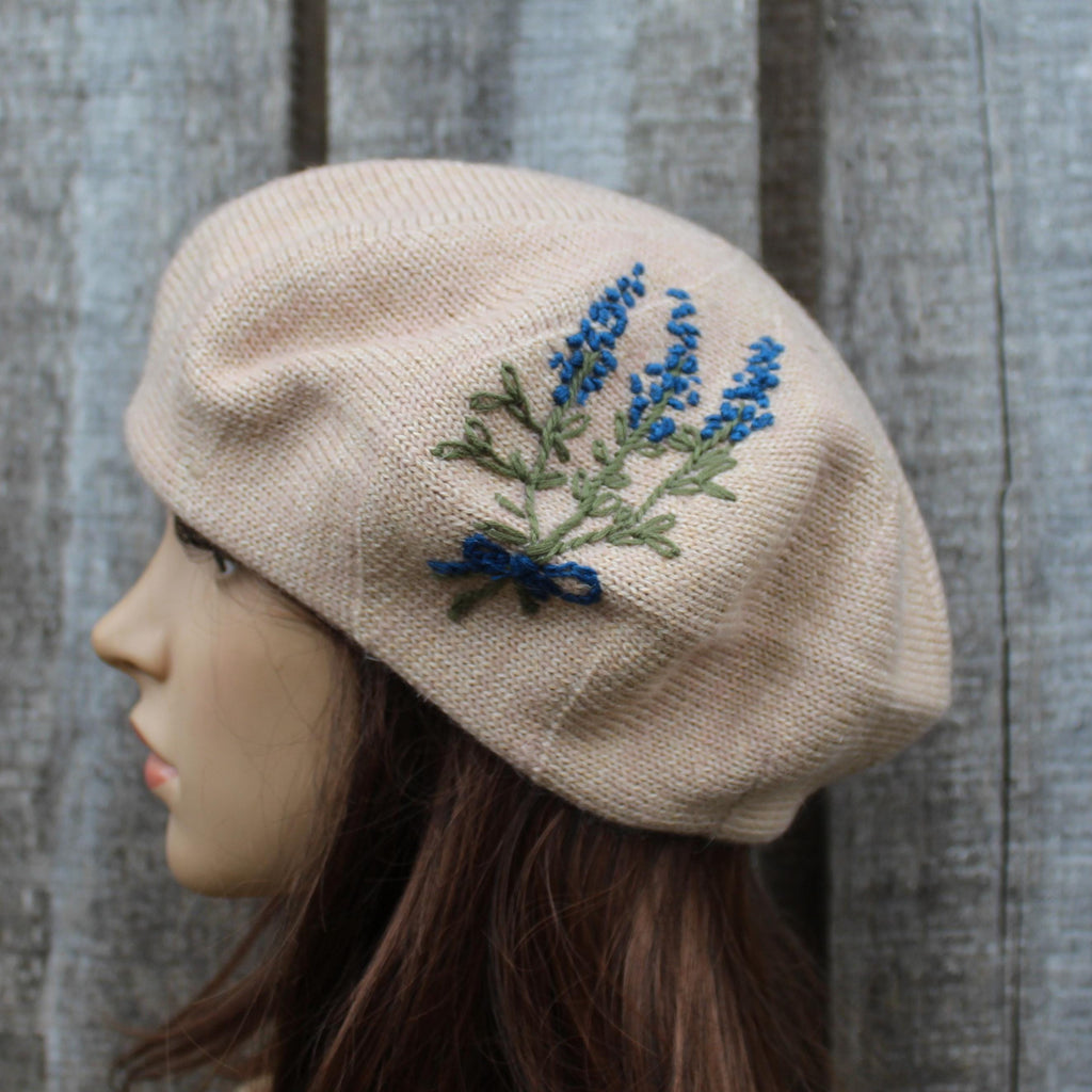Beige knit beret with embroidered blue flowers on a wooden background