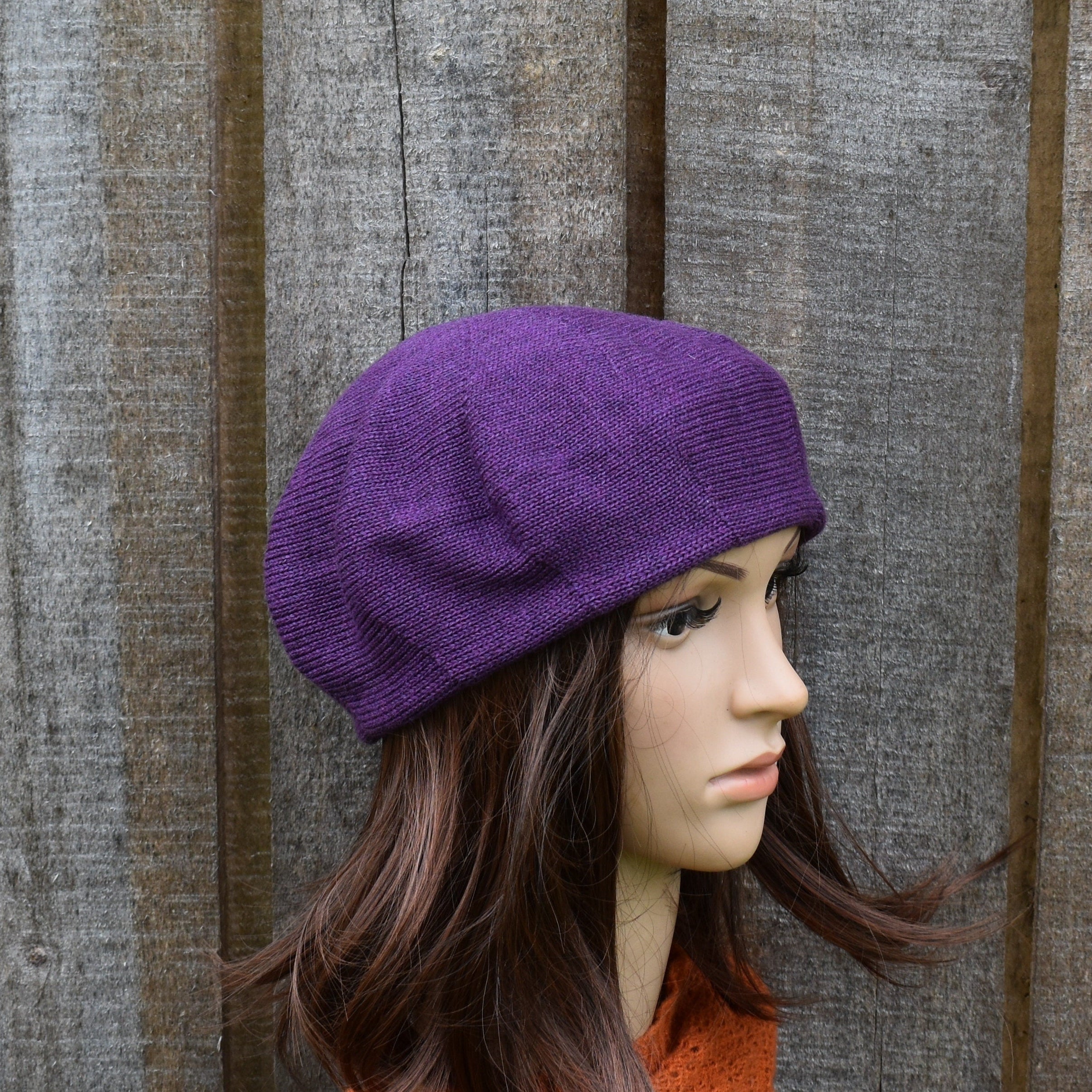 Mannequin head wearing a purple knit hat against a wooden background