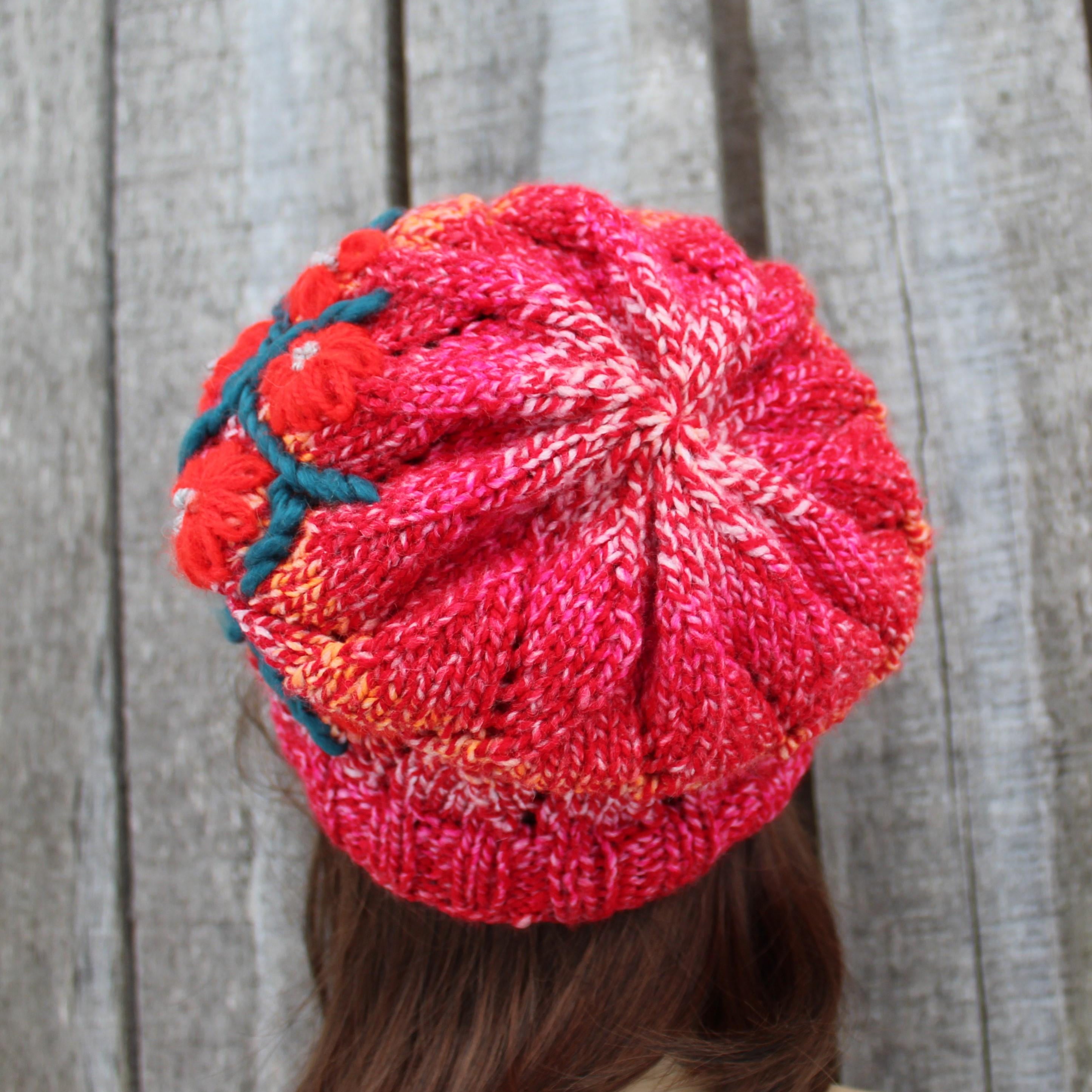 Red knitted beanie with a green detail on a wooden background