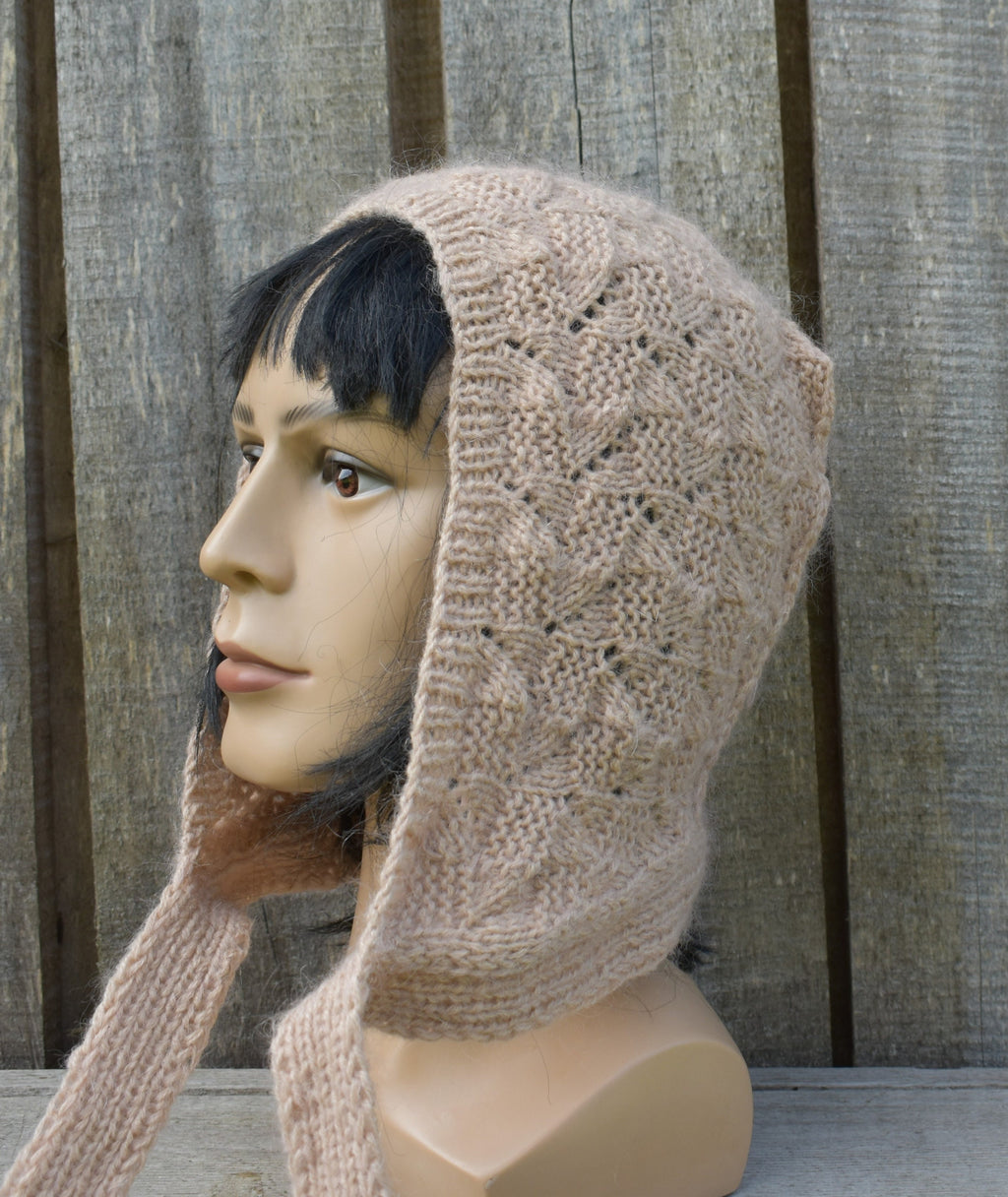 Mannequin head wearing a beige knitted hood against a wooden fence background