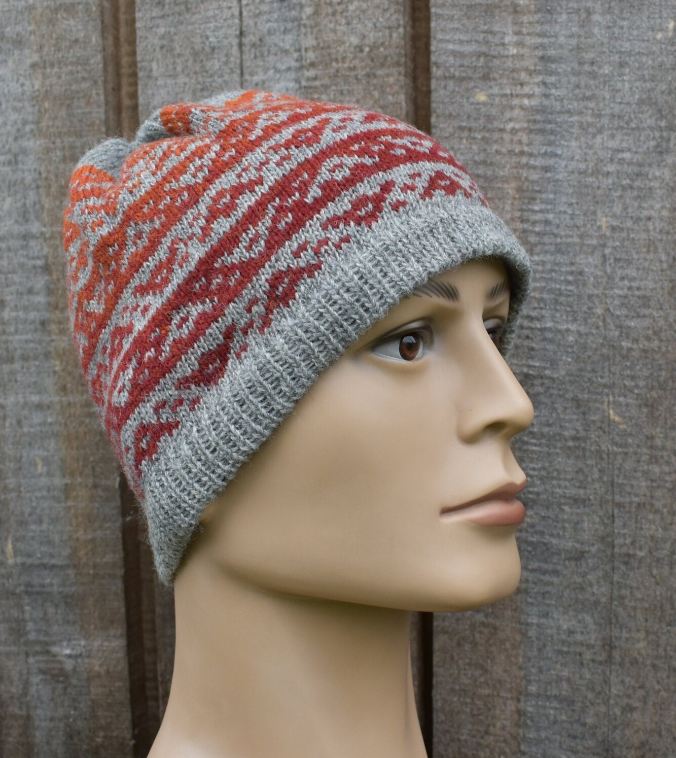 Knitted hat with red and gray pattern on a mannequin head against a wooden background